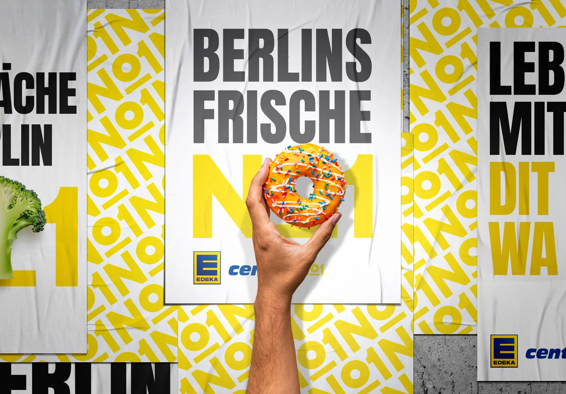 EDEKA No1: Ein Hand hält einen Donut mit Zuckerguss und bunten Streuseln vor einem Plakat mit dem Text „BERLINS FRISCHE N°1" und einem Edeka-Logo, im Hintergrund weitere Plakate mit ähnlichem Design.
