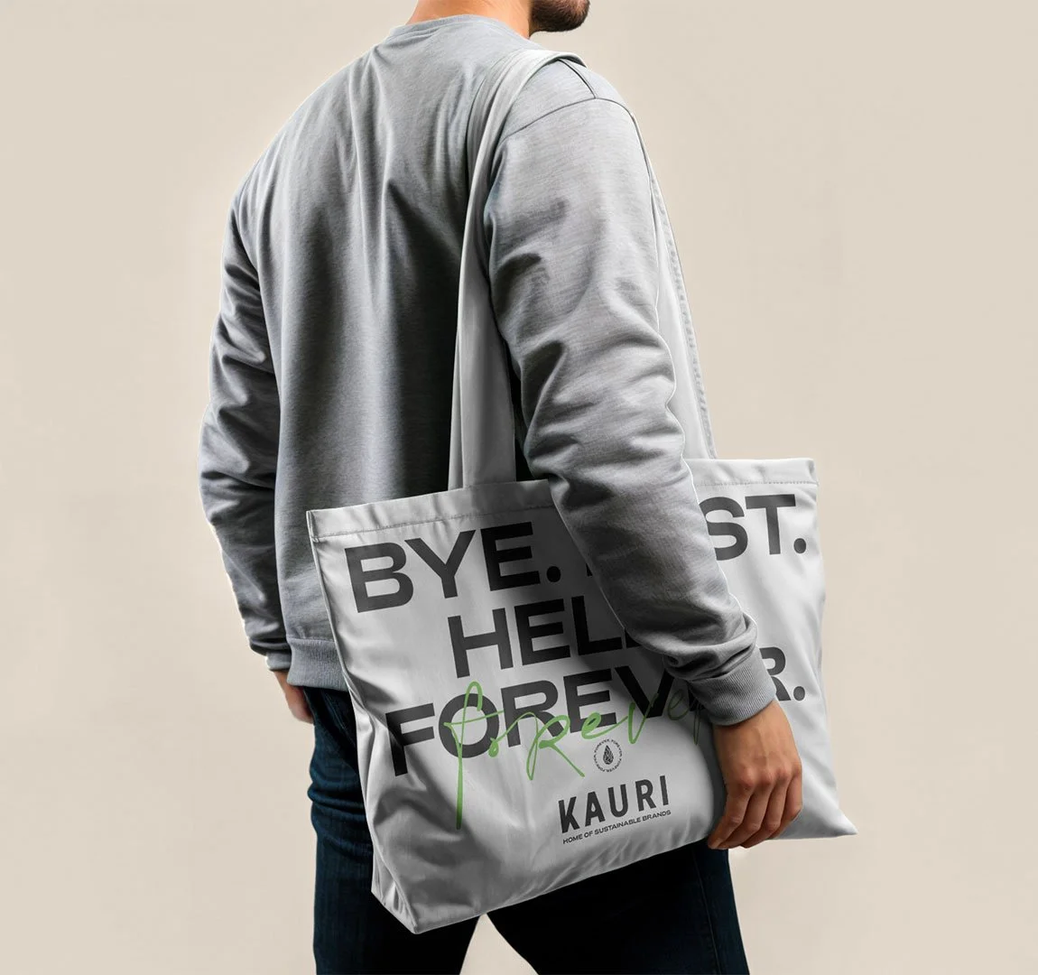 Person hält eine große weiße Tasche mit schwarzen und grünen Texten, trägt einen grauen Pullover, und der Hintergrund ist beige.