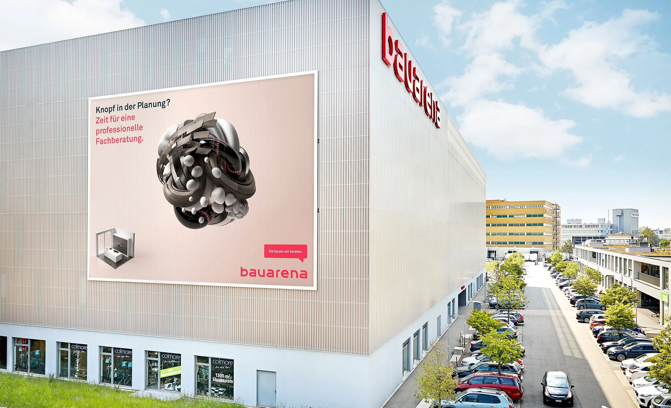Großes Plakat an einem Gebäude mit Werbung für professionelle Beratung bei Küchenplanung. Das Gebäude gehört zur bauarena. Der Himmel ist teilweise bewölkt, es befinden sich zahlreiche geparkte Autos und kleine Bäume entlang der Straße.