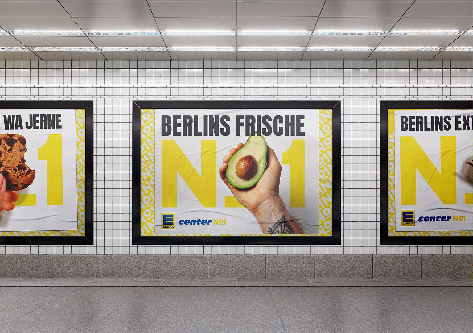 EDEKA No1 - Werbung in einer U-Bahn-Station mit einem Plakat, das eine halbe Avocado mit einem Tattoo zeigt. Das Plakat trägt den Text 'BERLINS FRISCHE' und 'N°1' in großen gelben Buchstaben, mit dem Logo von EDEKA und 'center N°1' am unteren Rand.