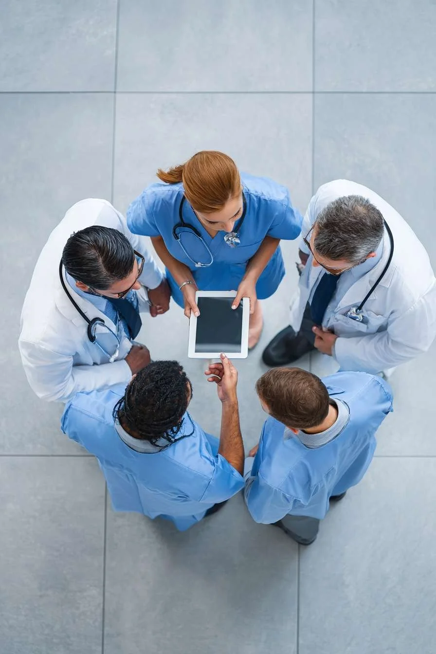 Group of healthcare professionals standing in a circle, looking at a tablet, taken from above