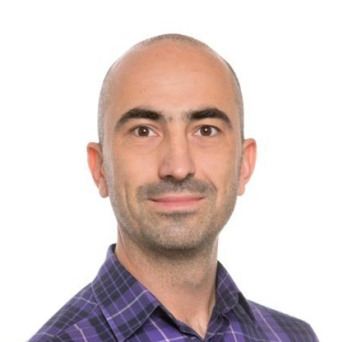 Headshot of a man with a shaved head, wearing a purple plaid shirt, against a white background.