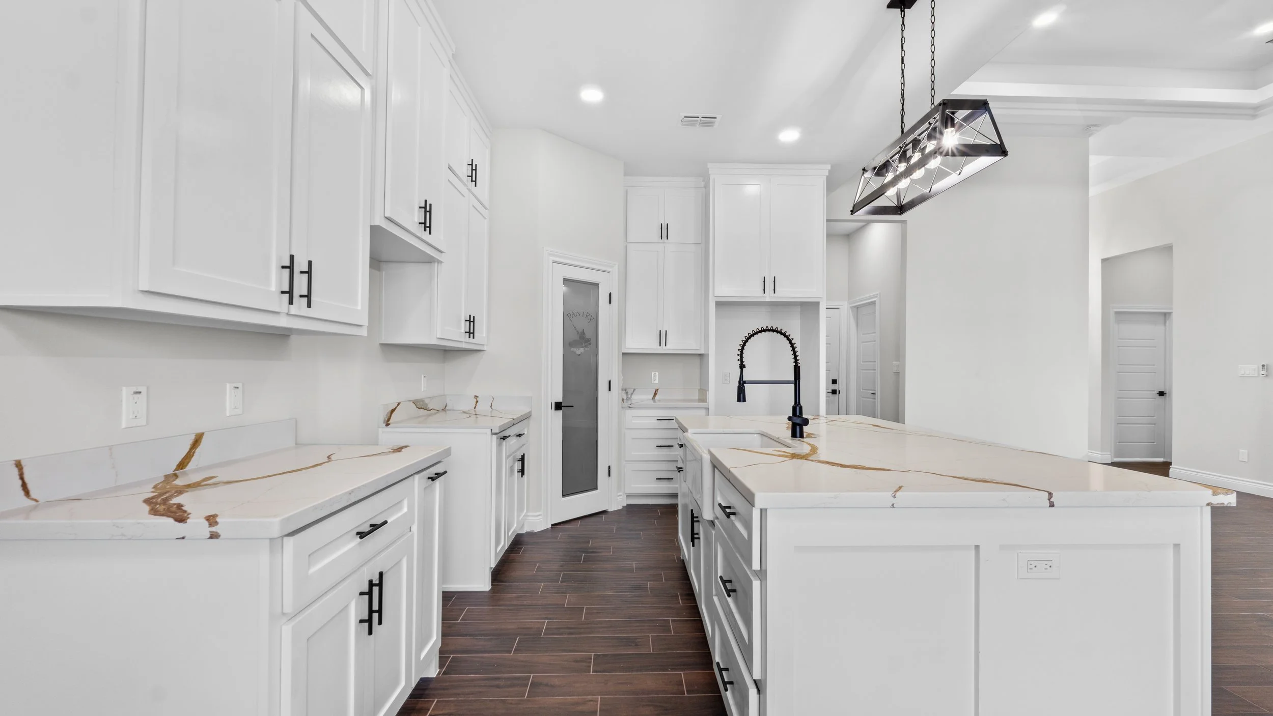 Cocina moderna con gabinetes blancos, encimera de mármol con vetas doradas, grifo negro en isla central y suelo de madera oscura.