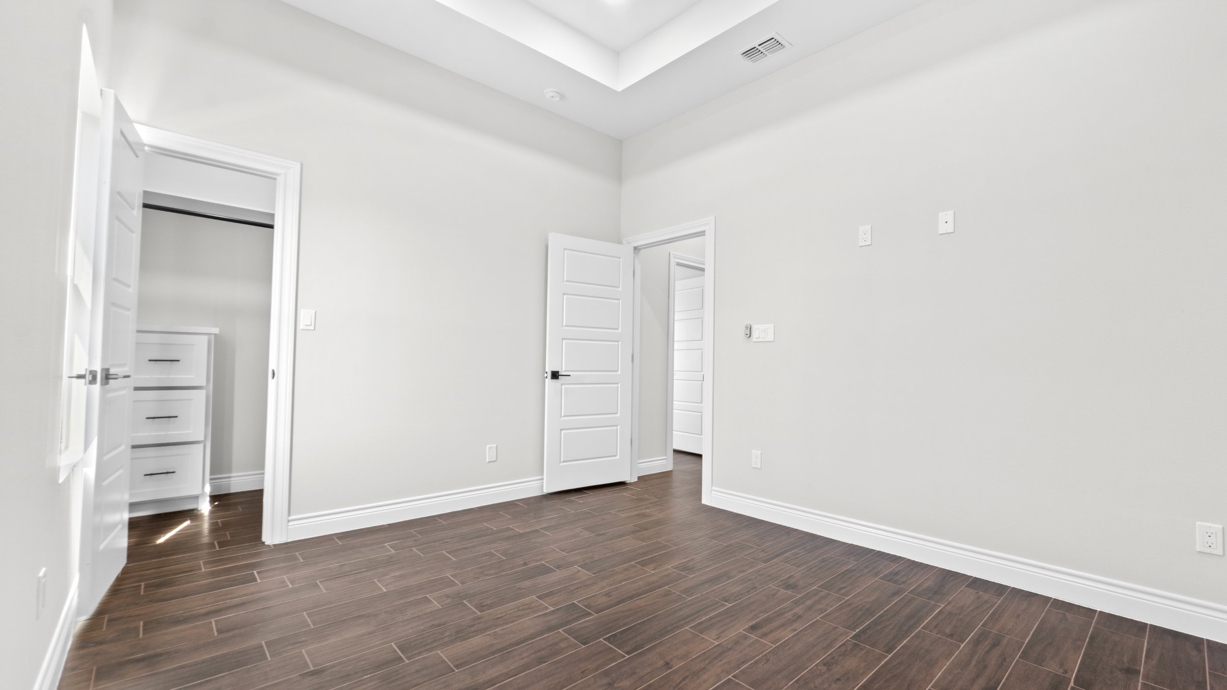 Habitación vacía con paredes blancas, piso de madera y puertas blancas abiertas.