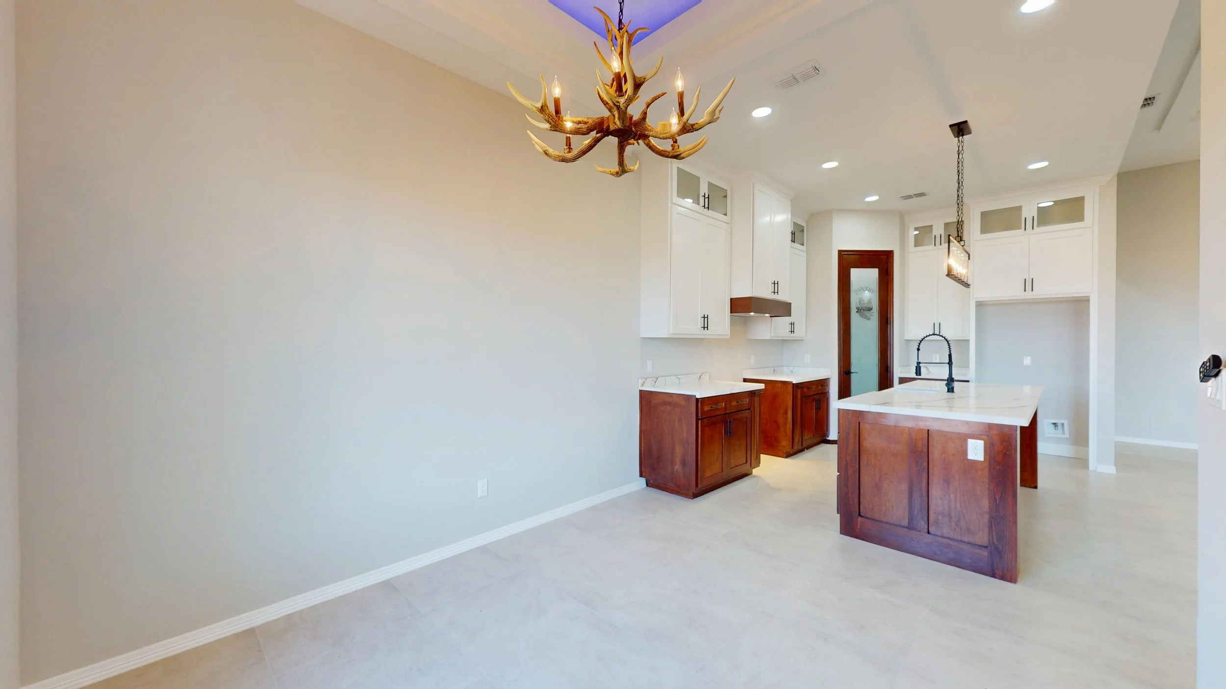 Cocina moderna con gabinetes blancos y de madera, isla con superficie de mármol, luz de candelabro de antorcha, iluminación empotrada en el techo, puerta de madera con vidrio, y encimera de granito, en espacio abierto y luminoso.