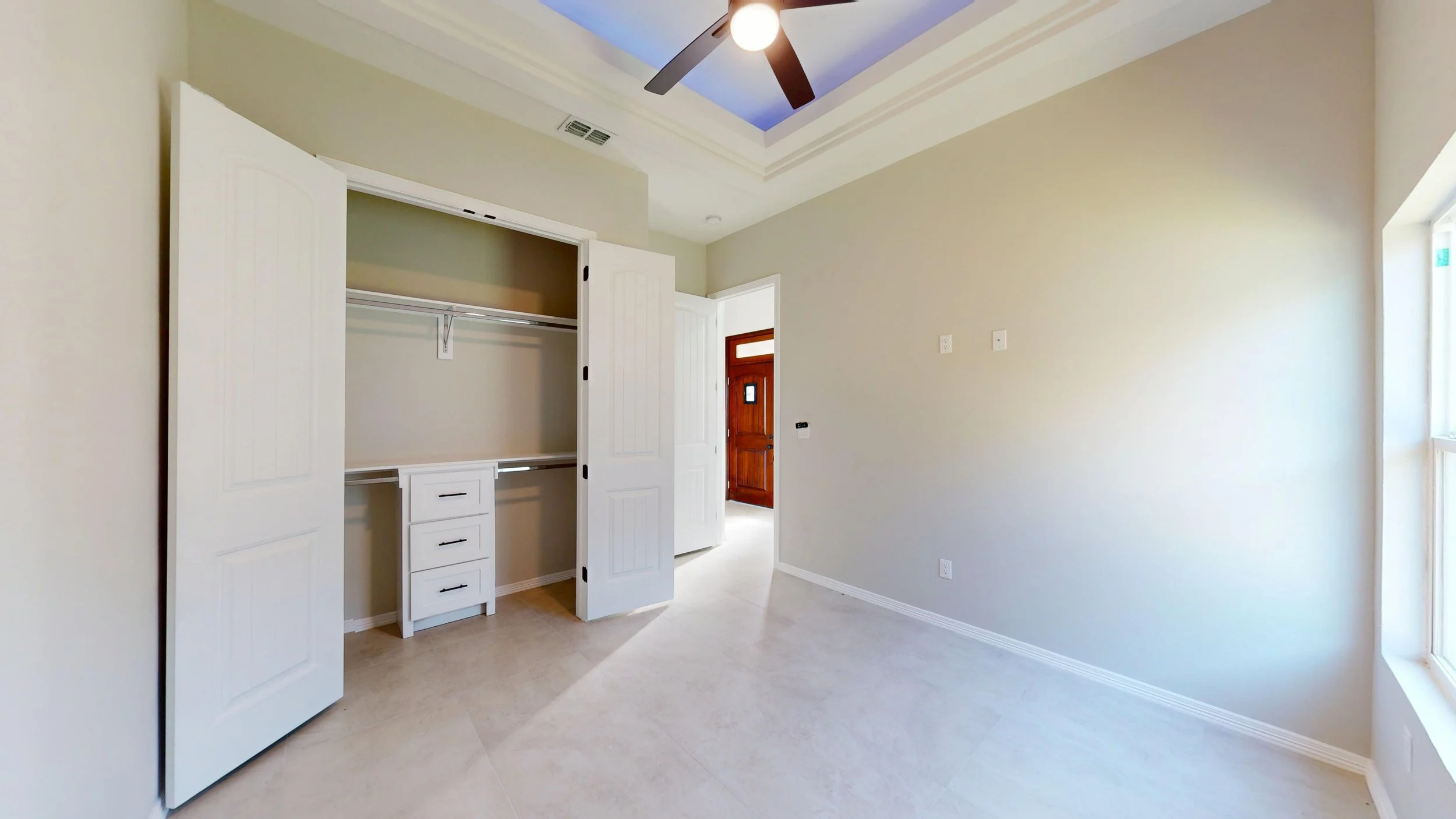 Habitat interior de una habitación vacía con armario empotrado y ventana, puertas blancas y suelo de baldosas.