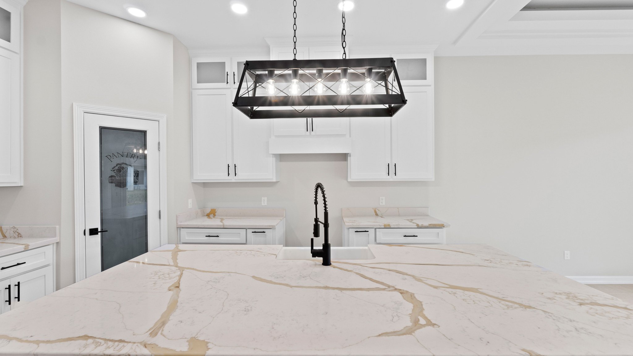 Cocina moderna con encimera de mármol y mobiliario blanco, lámpara colgante negra y grifo negro en el fregadero centro.