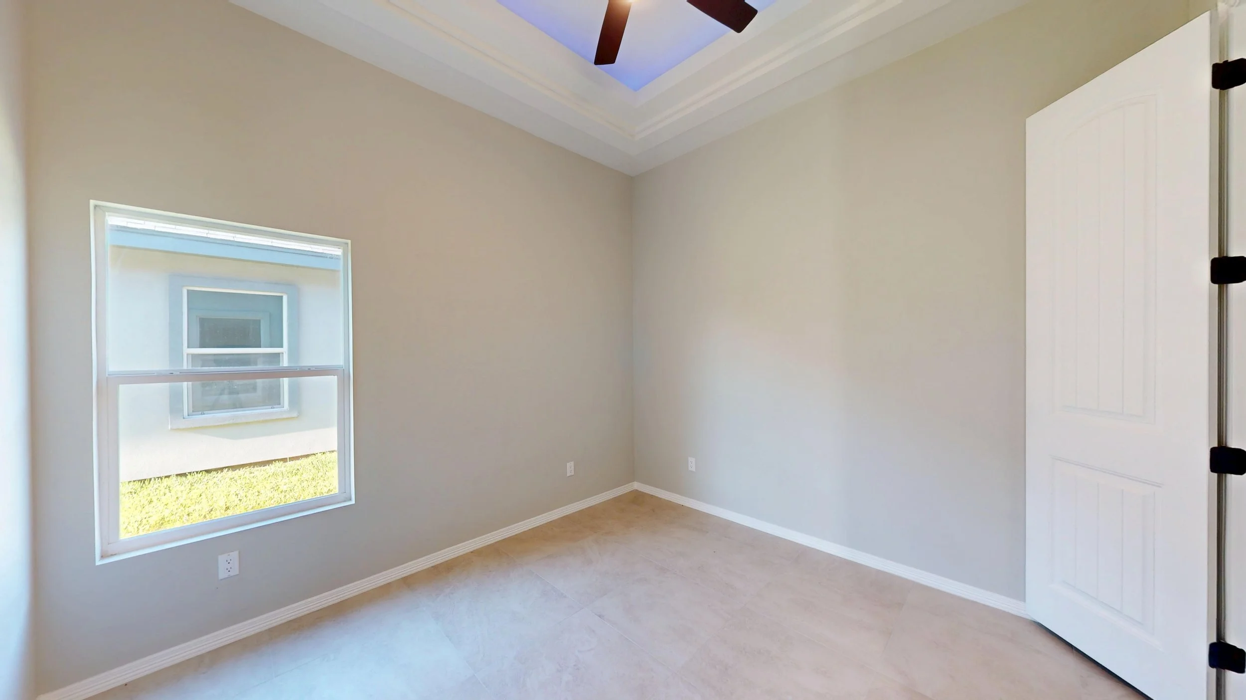 Cuarto vacío con una ventana y una puerta blanca, paredes beige y suelo de baldosas.