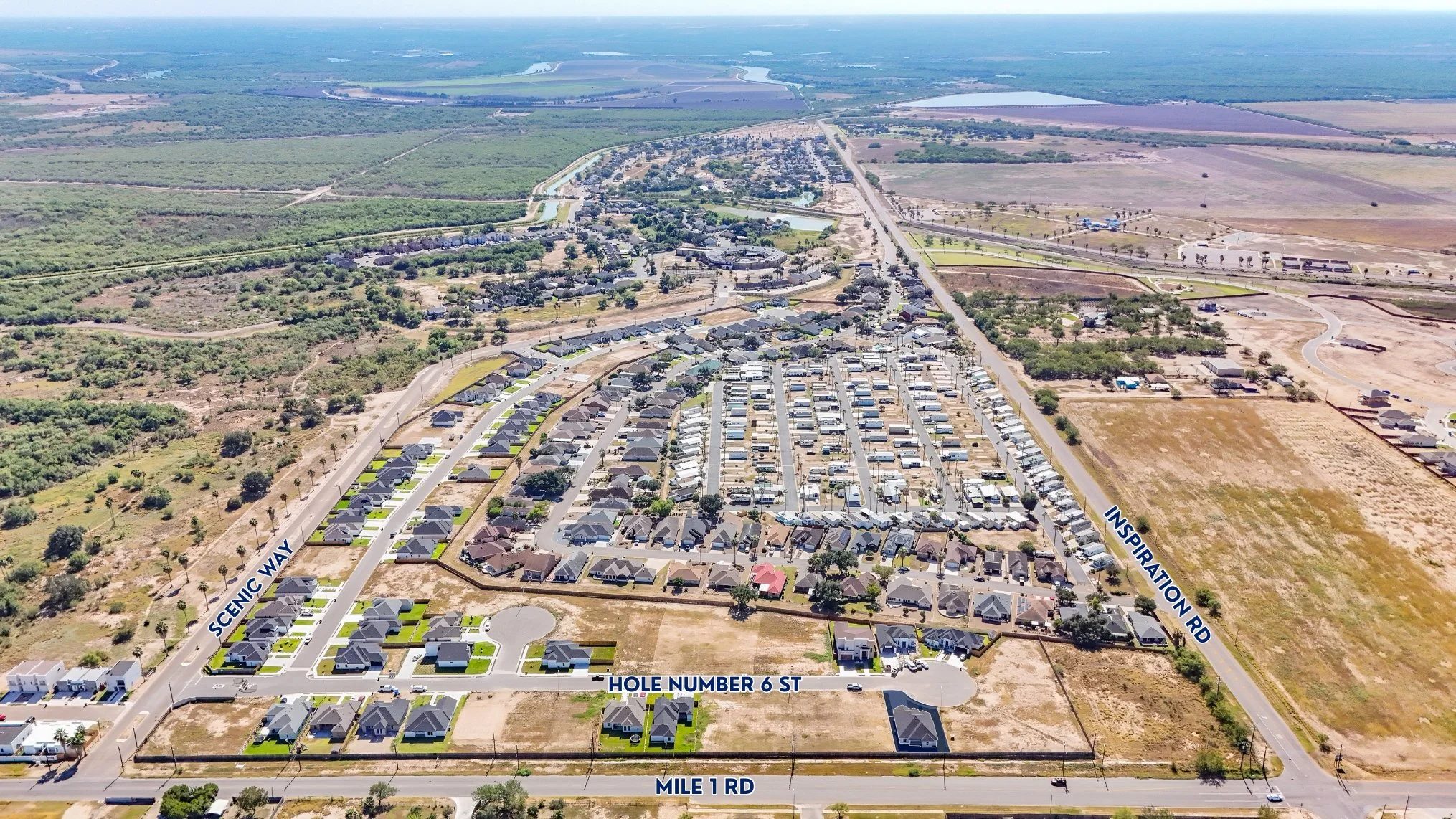 Vista aérea de un vecindario en un área rural con calles, casas, y terrenos abiertos, con etiquetas que indican las calles Scenic Way, Inspiration Rd, Hole Number 6 St y Mile 1 Rd.
