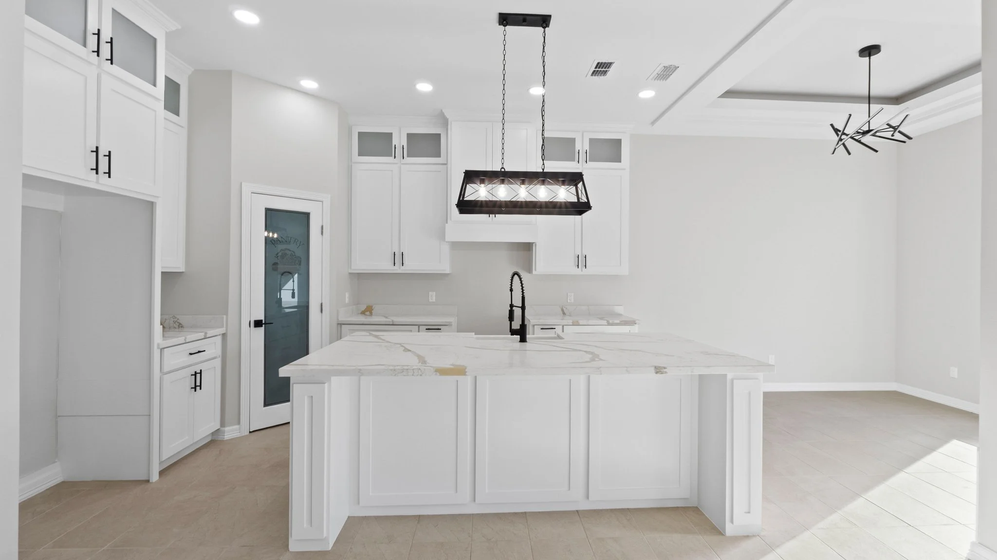 Cocina moderna con isla central de mármol blanco, gabinetes blancos, y luz colgante negra en el techo.