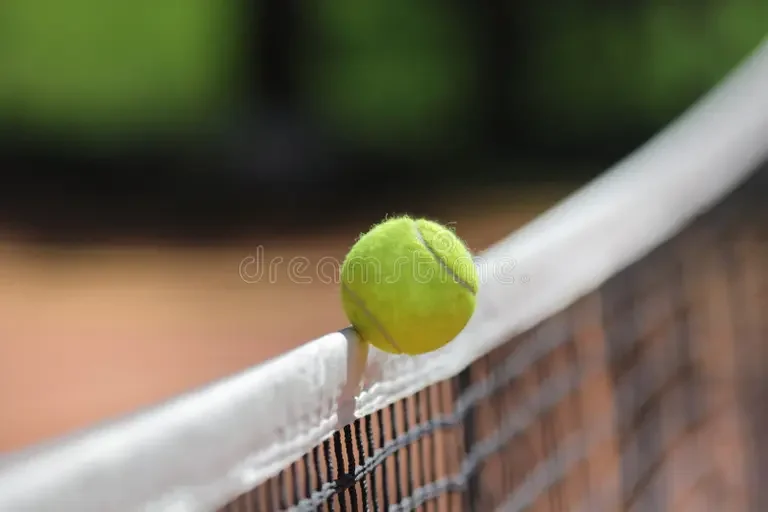 A green tennis ball resting on the net of a tennis court.