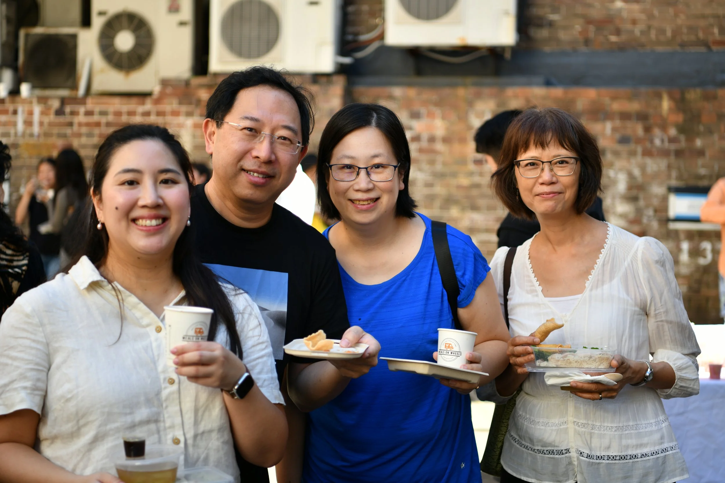 Four adults smiling whilst holding plates and cups.