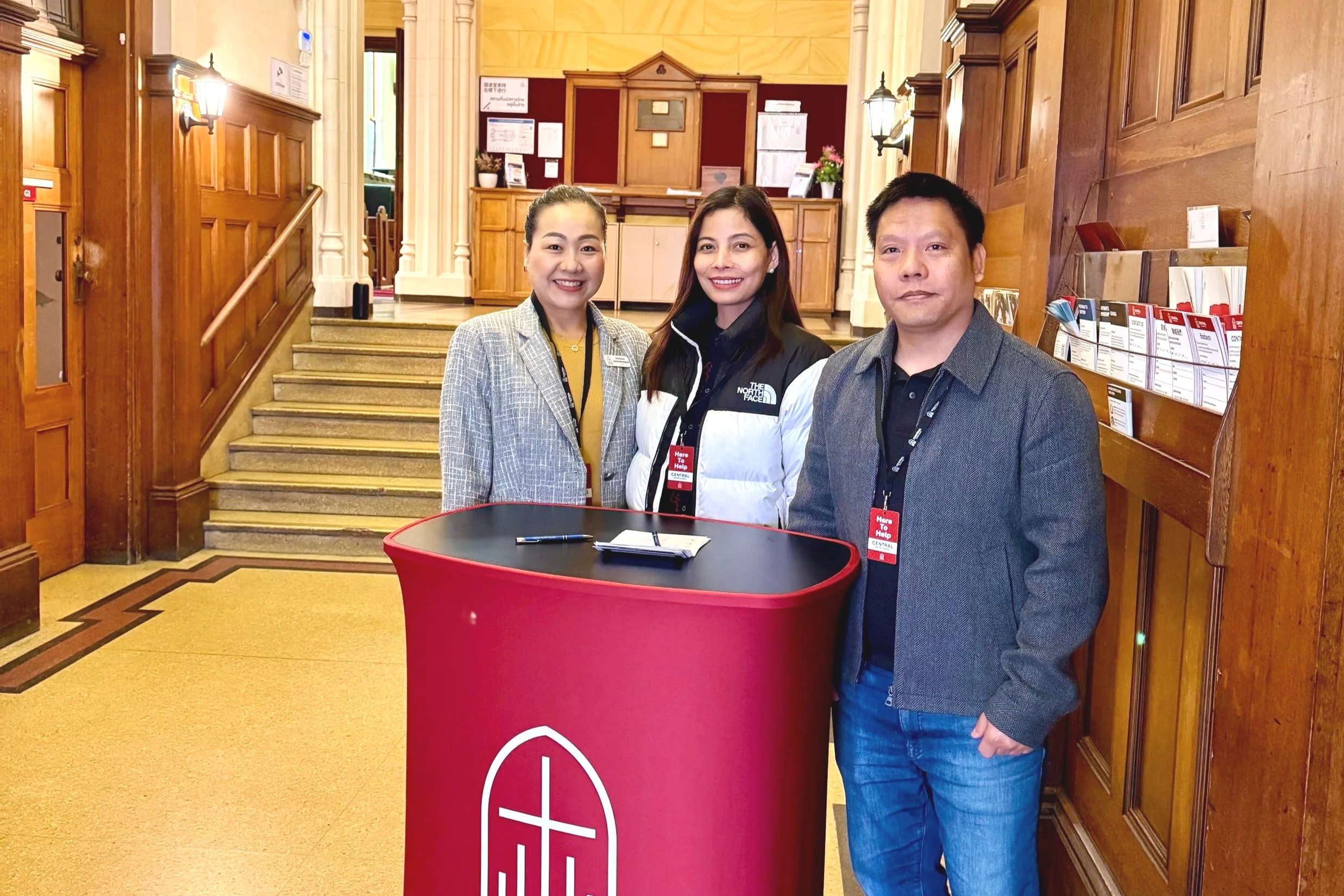 Three people standing behind a welcoming desk.