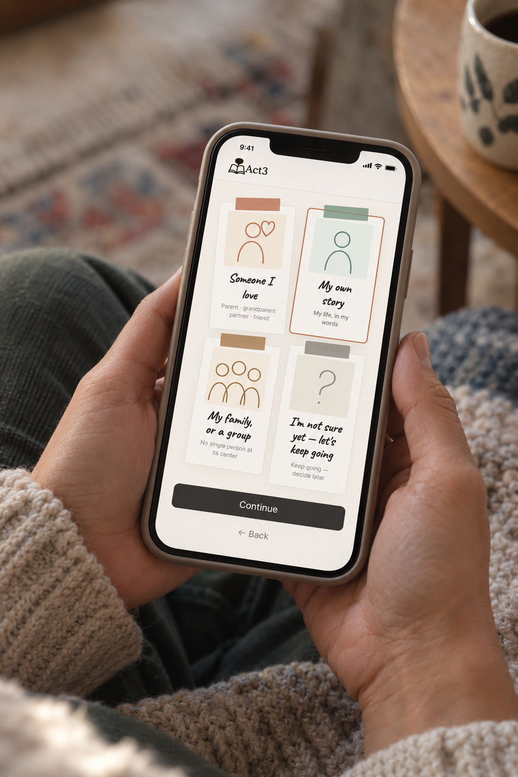 Hand holding a smartphone displaying a story creating app called Act3, with a question about the main character of a story and options to select 'Myself' or 'Someone else'.