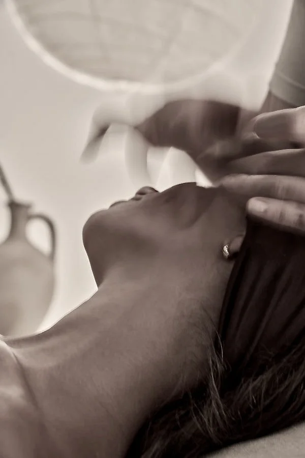 Close-up of a woman lying down with her hand gently touching her forehead, wearing an earring.