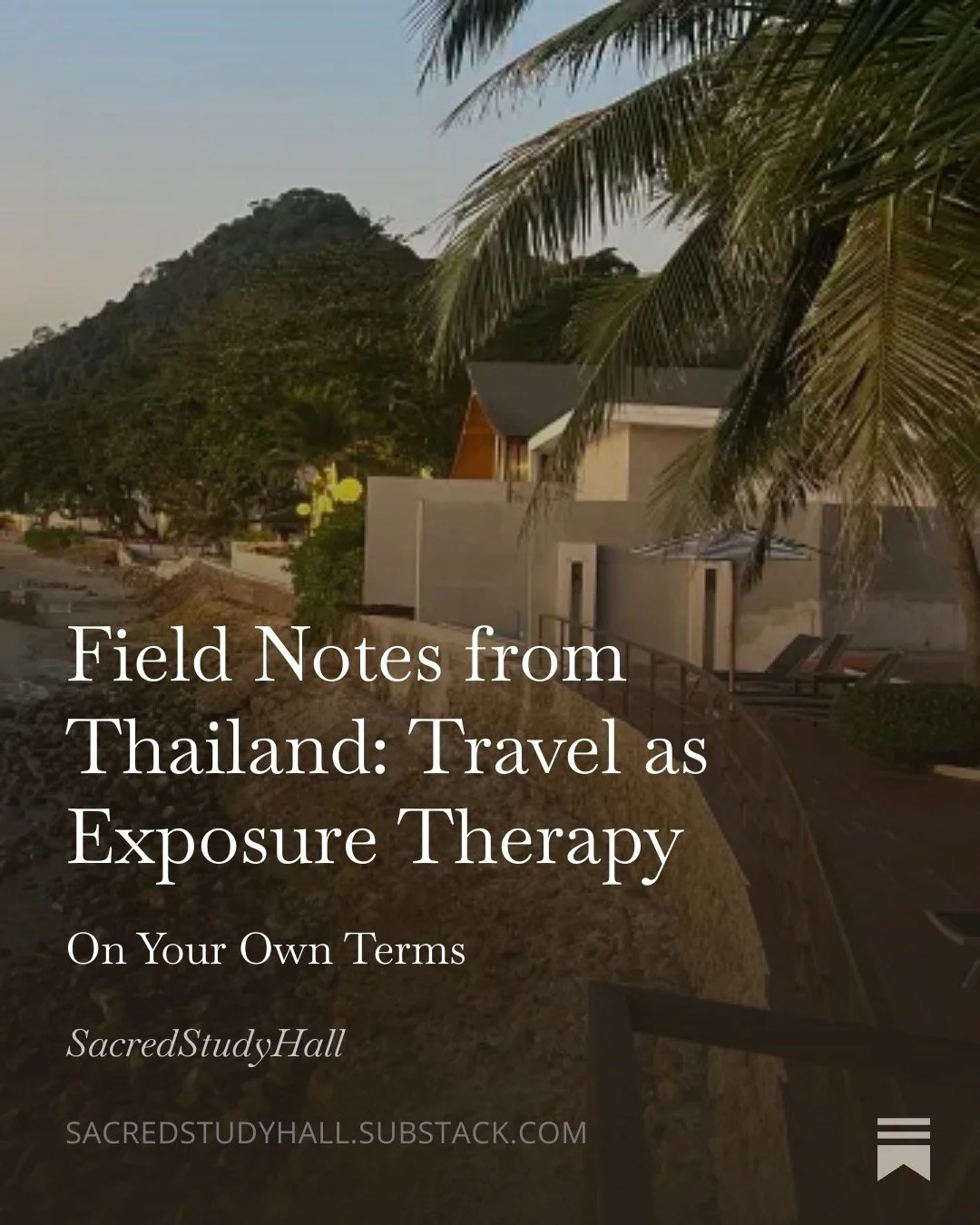 Sunset view of a street with modern white buildings, palm trees, a mountain in the background, and a pathway with lounge chairs.