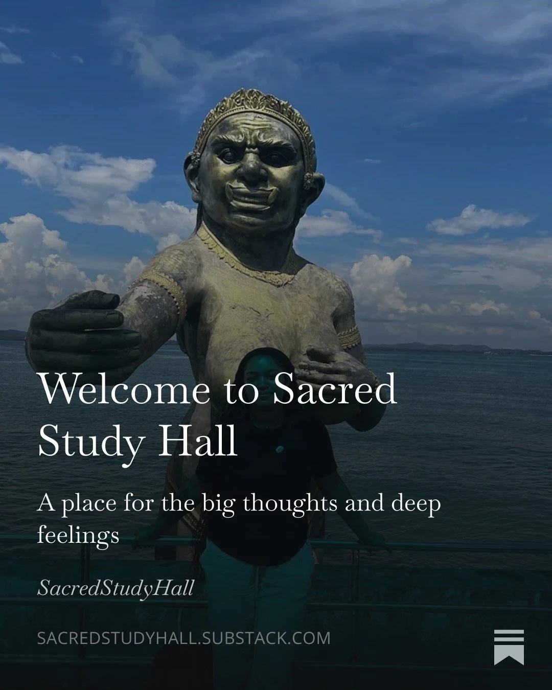 A large statue of a smiling, gesturing child with a crown on its head, set against a cloudy sky and body of water. A person stands in front of the statue.