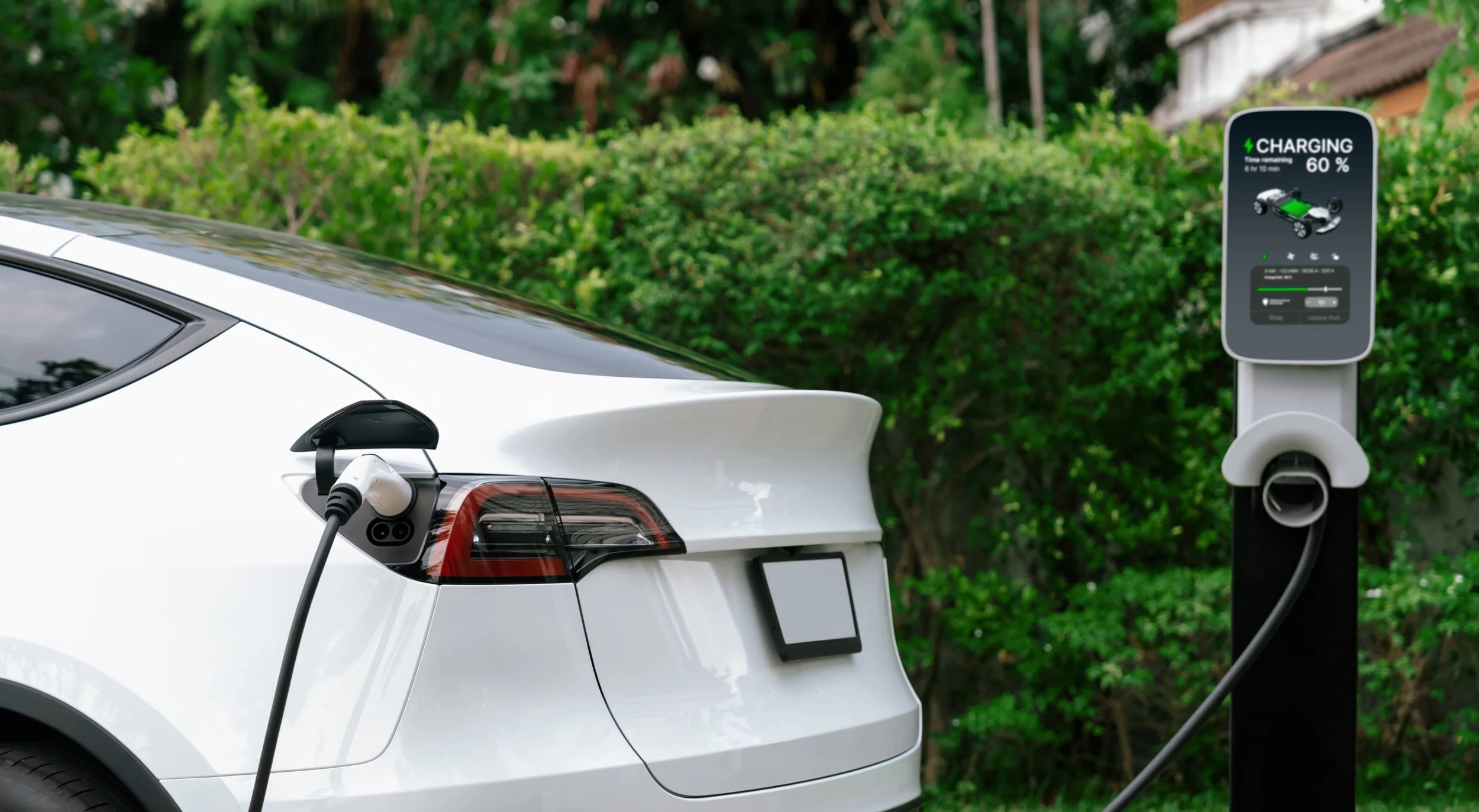 Voiture blanche en train de charger avec une station de recharge électrique dans un environnement verdoyant.