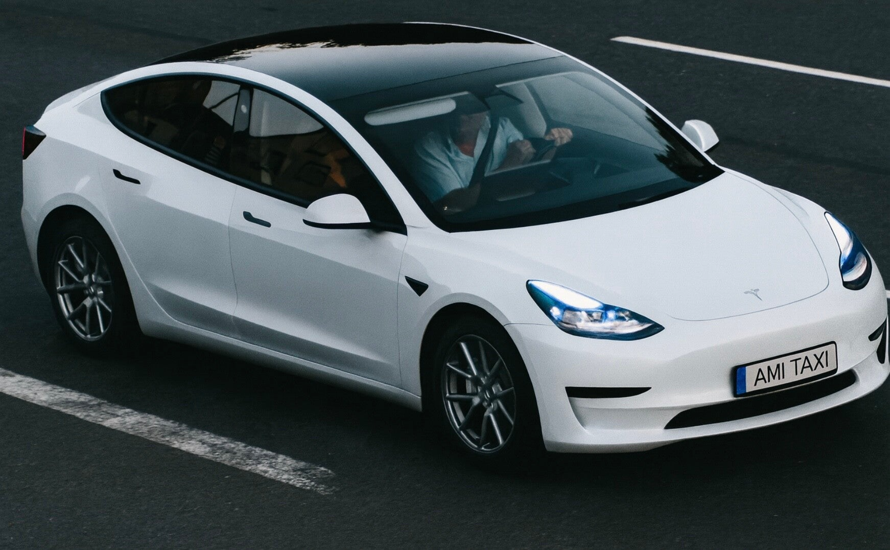 Voiture électrique blanche avec un chauffeur, porte-boutique "AMI TAXI", roulant sur une route