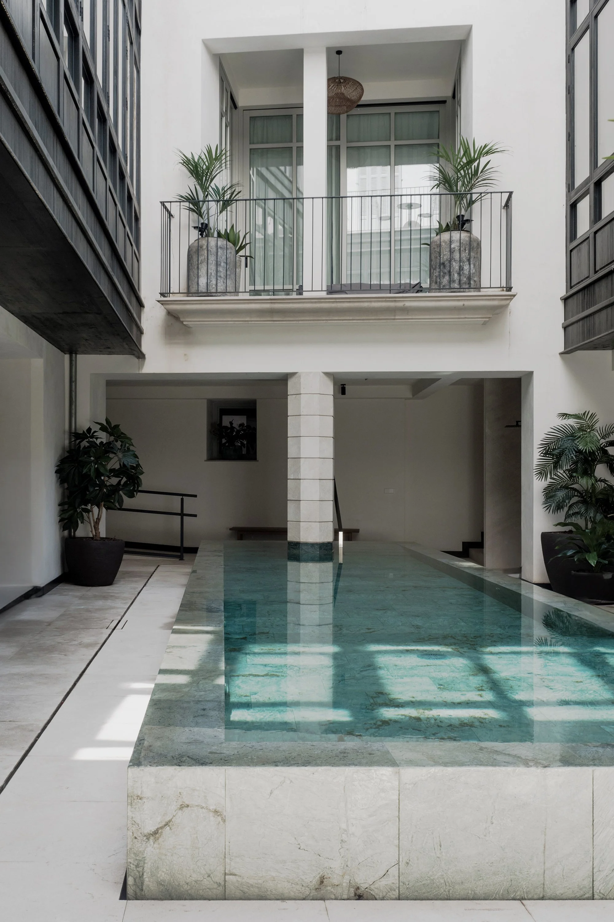 Indoor swimming pool with clear blue water, surrounded by white marble tiles and potted plants.
