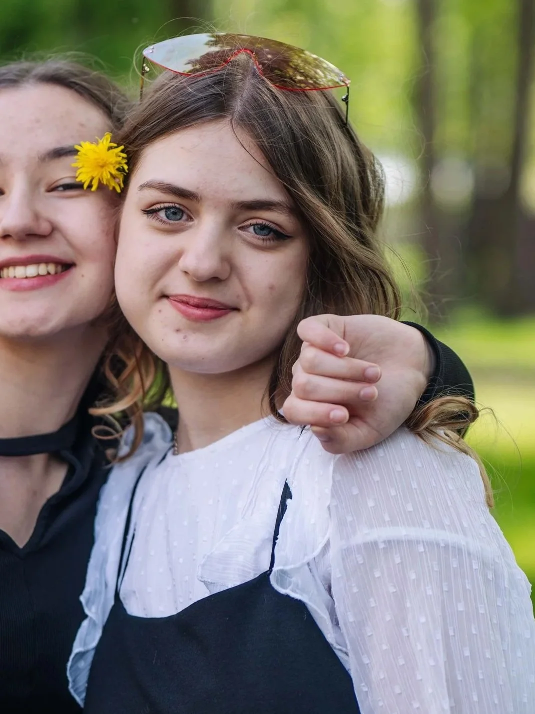 Two young women smiling outdoors, one with a yellow flower in her hair.
