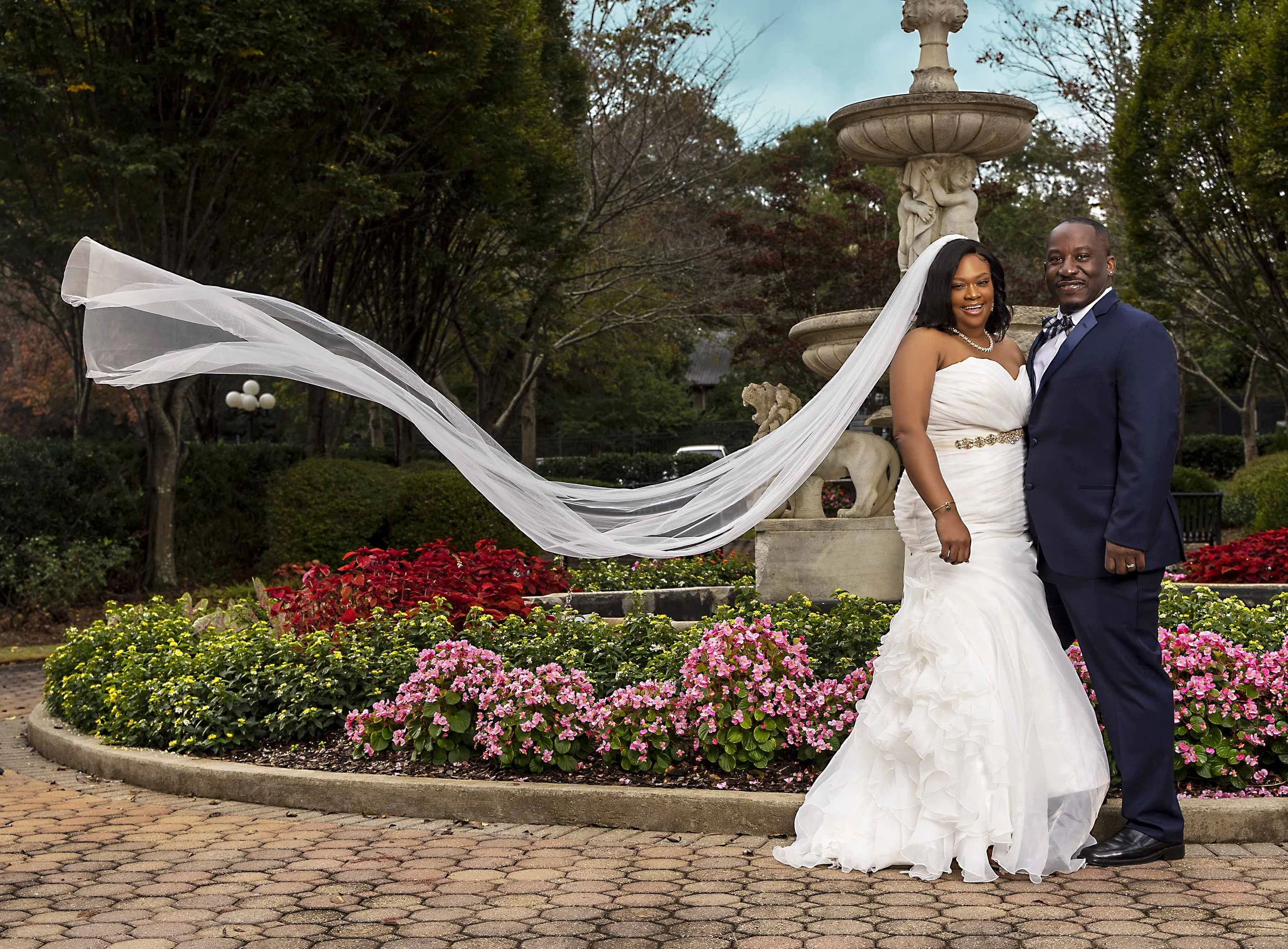 Wedding photo bride and groom in front of fountain. veil flowing in the air
