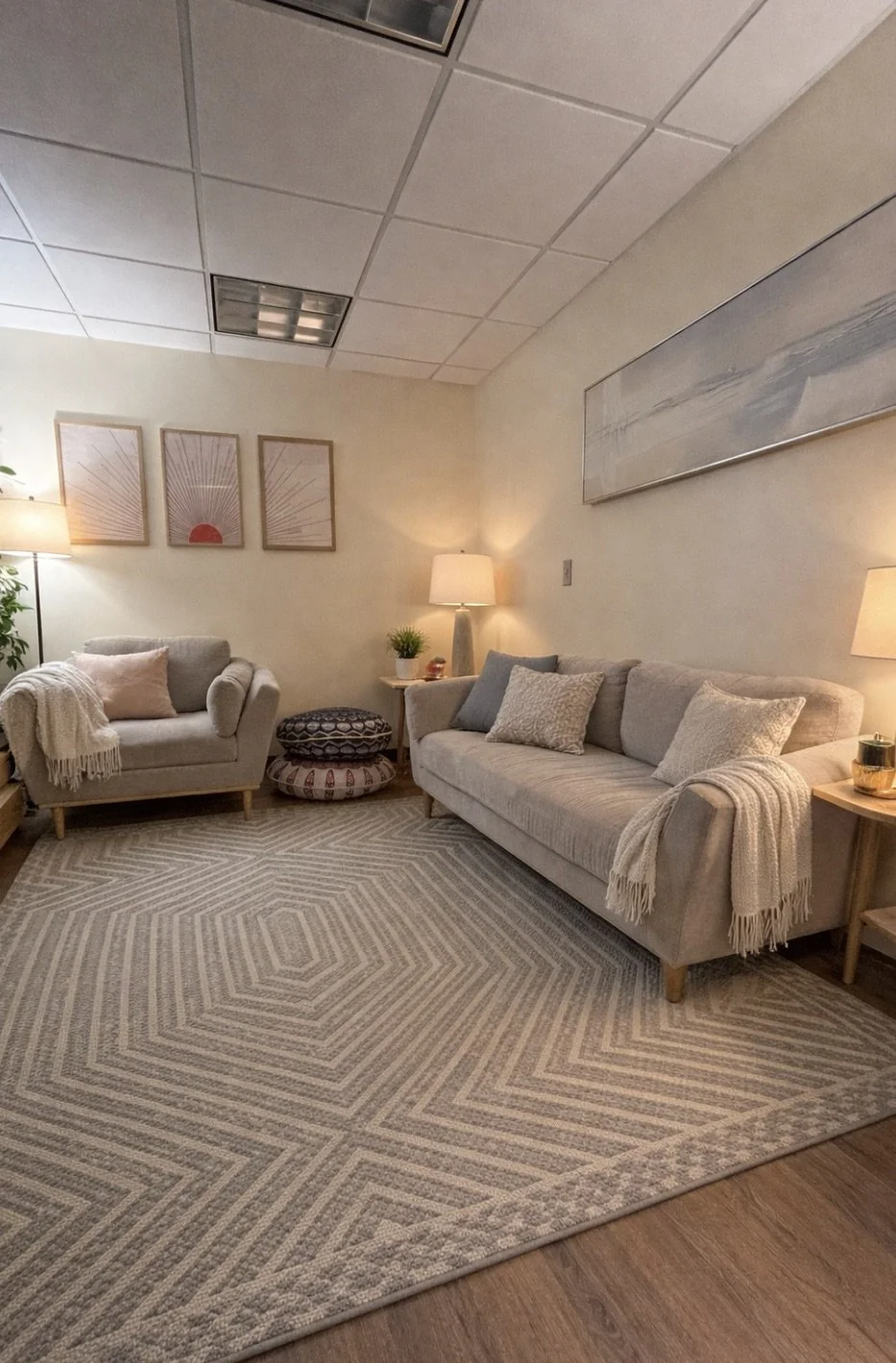 A cozy living room with two beige sofas, cushions, a patterned rug, side tables with lamps, wall art, and soft lighting.
