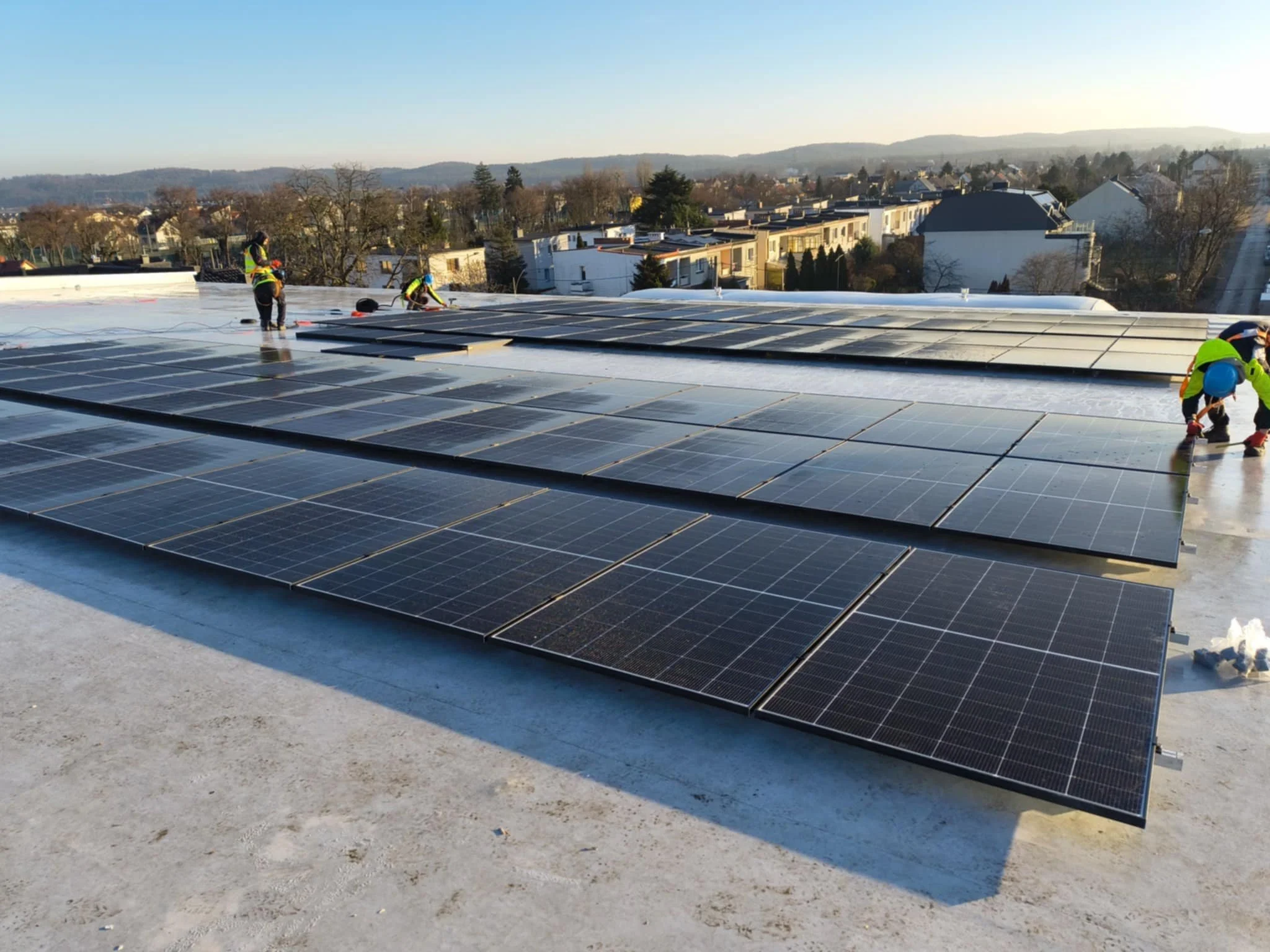 Workers installing solar panels on a rooftop during daytime with a cityscape in the background.