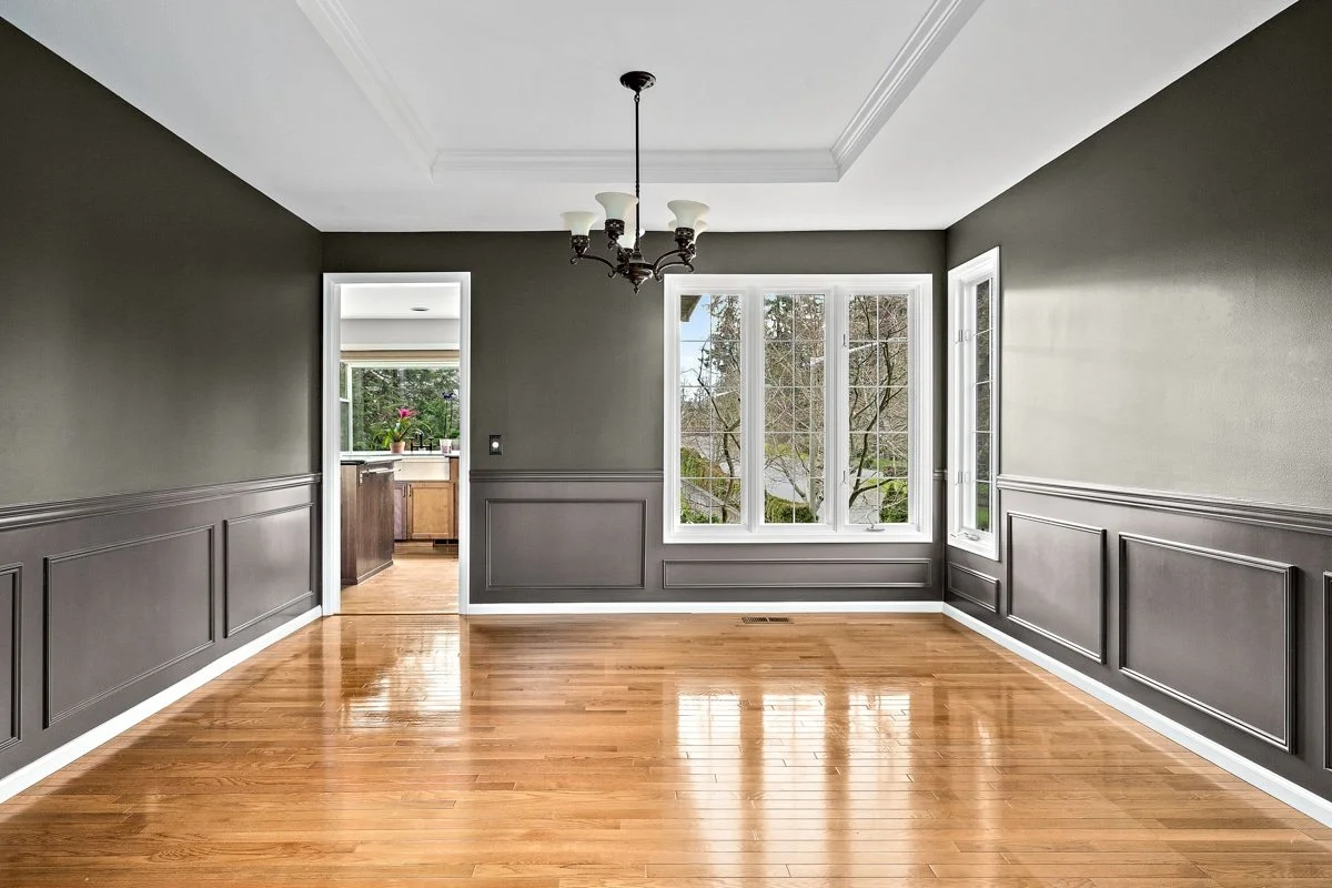Empty room with dark gray walls, wooden floor, large window, and chandelier.