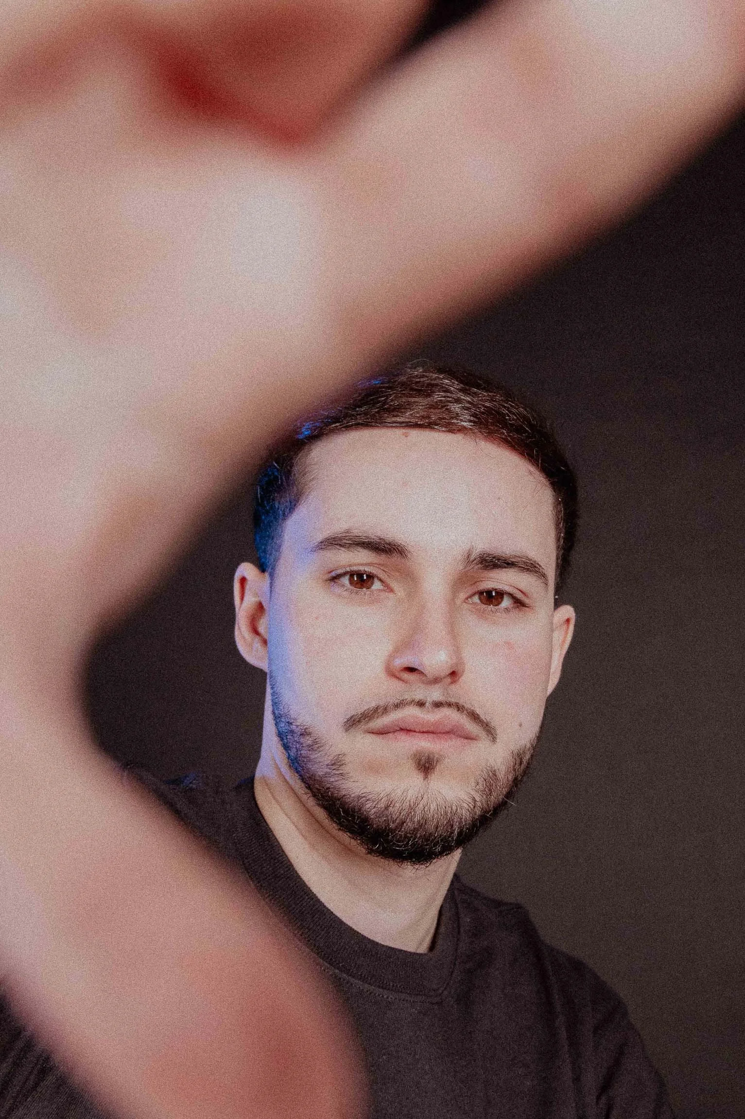 Ritratto di un giovane uomo con barba e capelli corti, che guarda verso la fotocamera, con uno sfondo nero e un'ombra sulla sua faccia.

© Alessandro Holneider