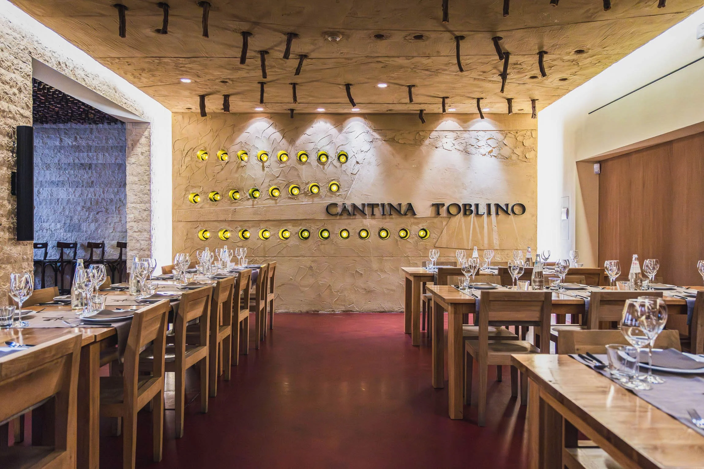 Interno di un ristorante elegante con tavoli apparecchiati con bicchieri e posate, parete con scaffale di bottiglie di vino e scritta 'Cantina Toblino'.
© Alessandro Holneider
