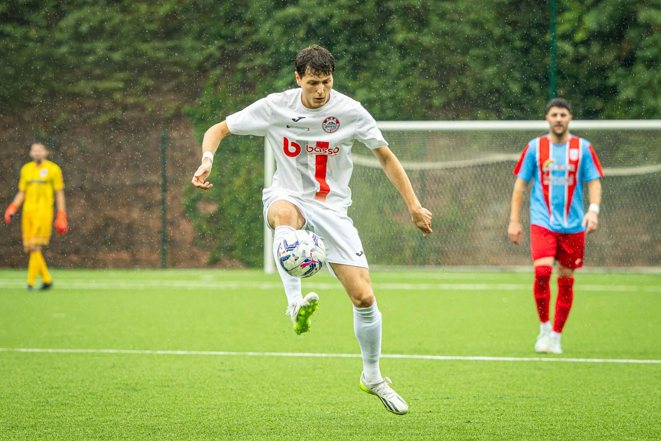 ASD Calisio Calcio. Giocatore di calcio in azione durante una partita sotto la pioggia, con un avversario sullo sfondo, in campo verde.

© Alessandro Holneider