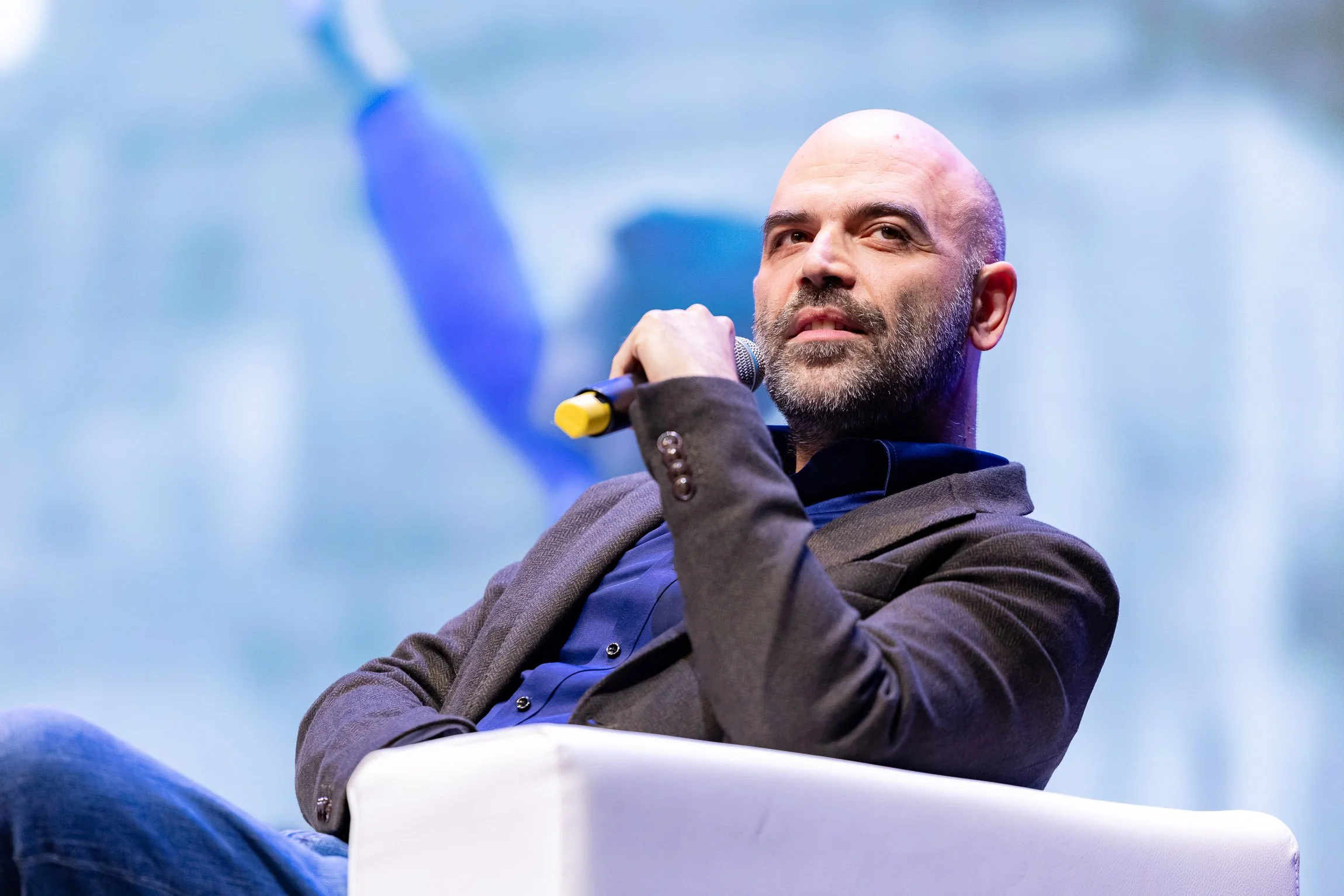 Saviano al Festival dello Sport di Trento. Uomo con barba che tiene un microfono mentre si trova in un evento o conferenza, con sfondo blu e illuminate

© Alessandro Holneider - Archivio Ufficio Stampa PAT