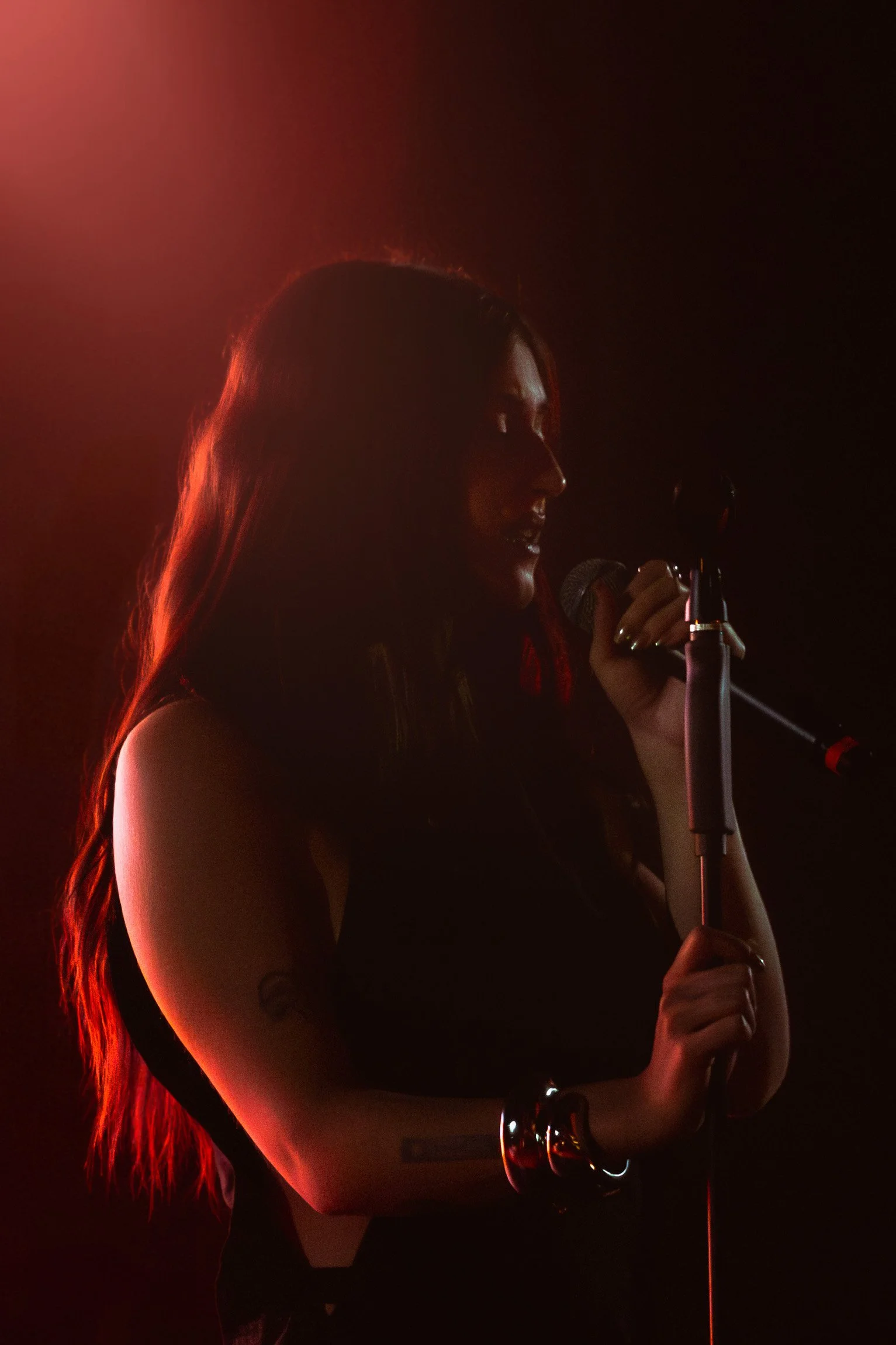 Donna con capelli lunghi che tiene un microfono in mano davanti a uno sfondo nero con un'illuminazione calda