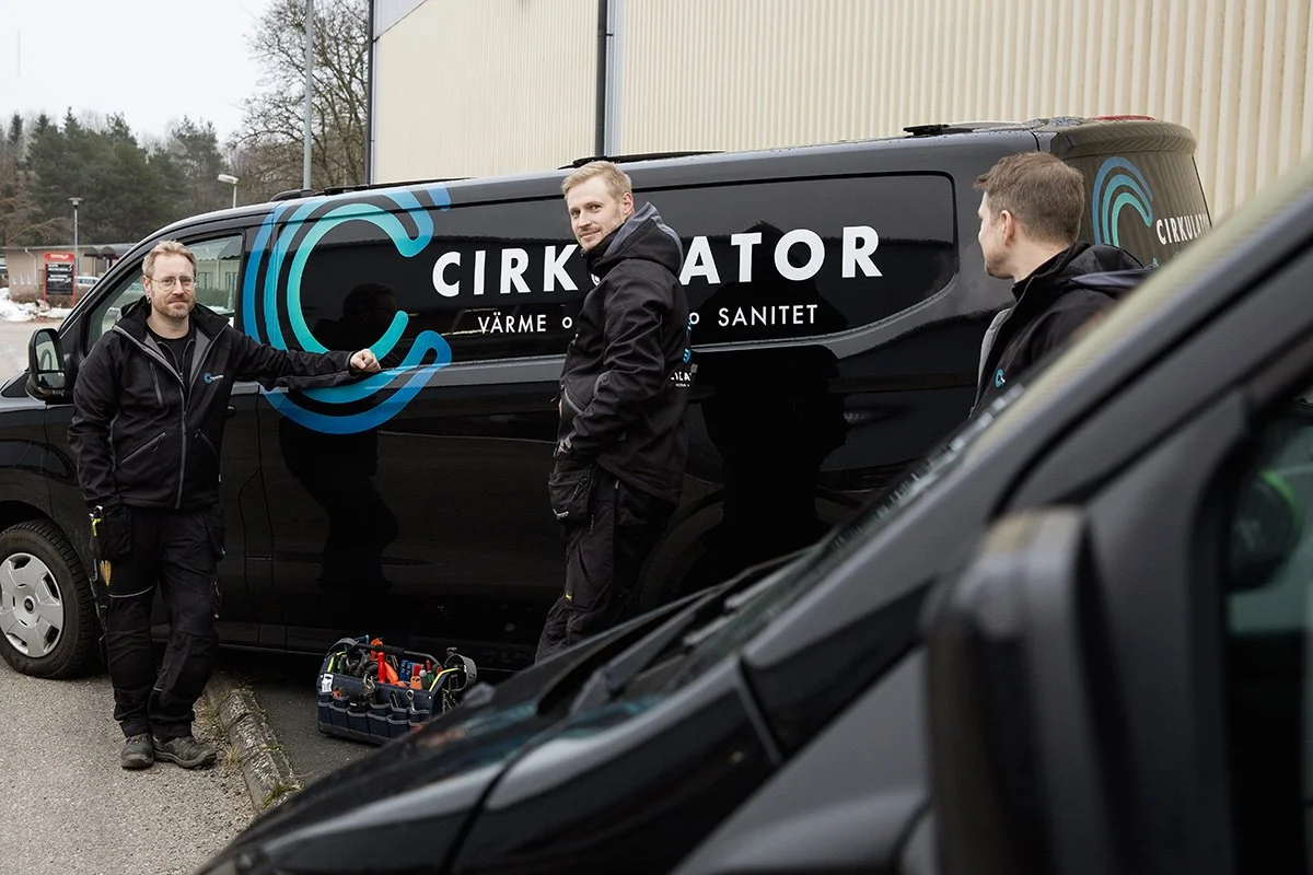Tre kollegor från ett VVS företag står bredvid en svart skåpbil utomhus med texten 'Cirkulator, Värme Vatten och Sanitet' på sidan.
