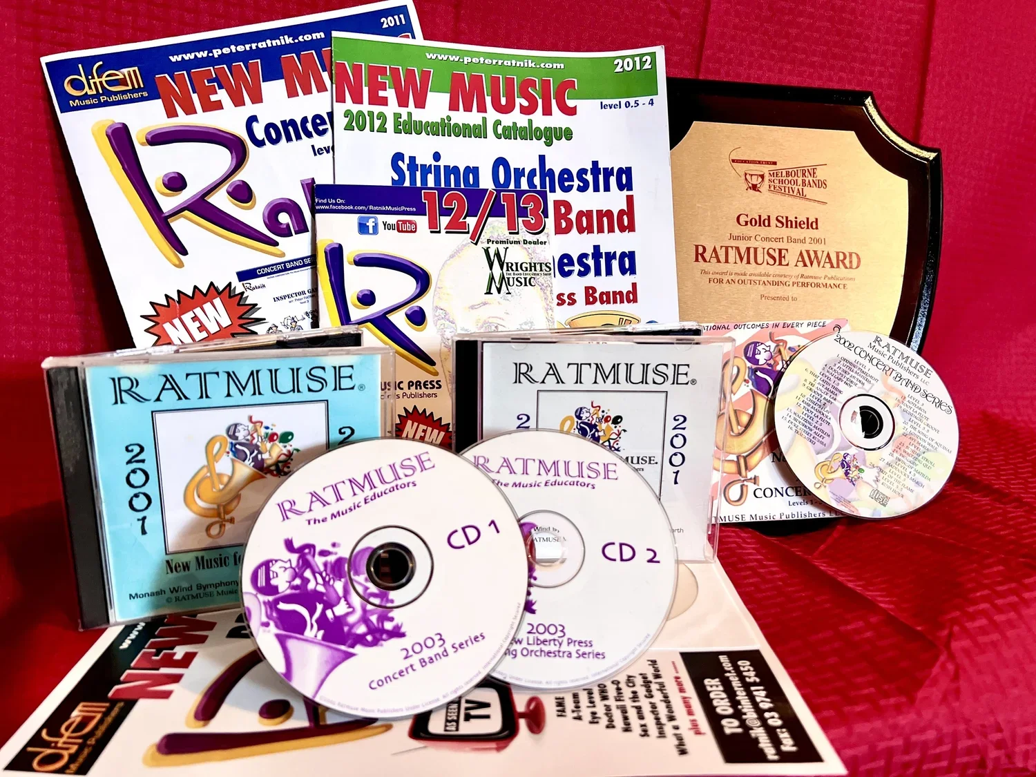 Music education materials, including CDs, booklets, and awards, with colorful publications and a red background.
