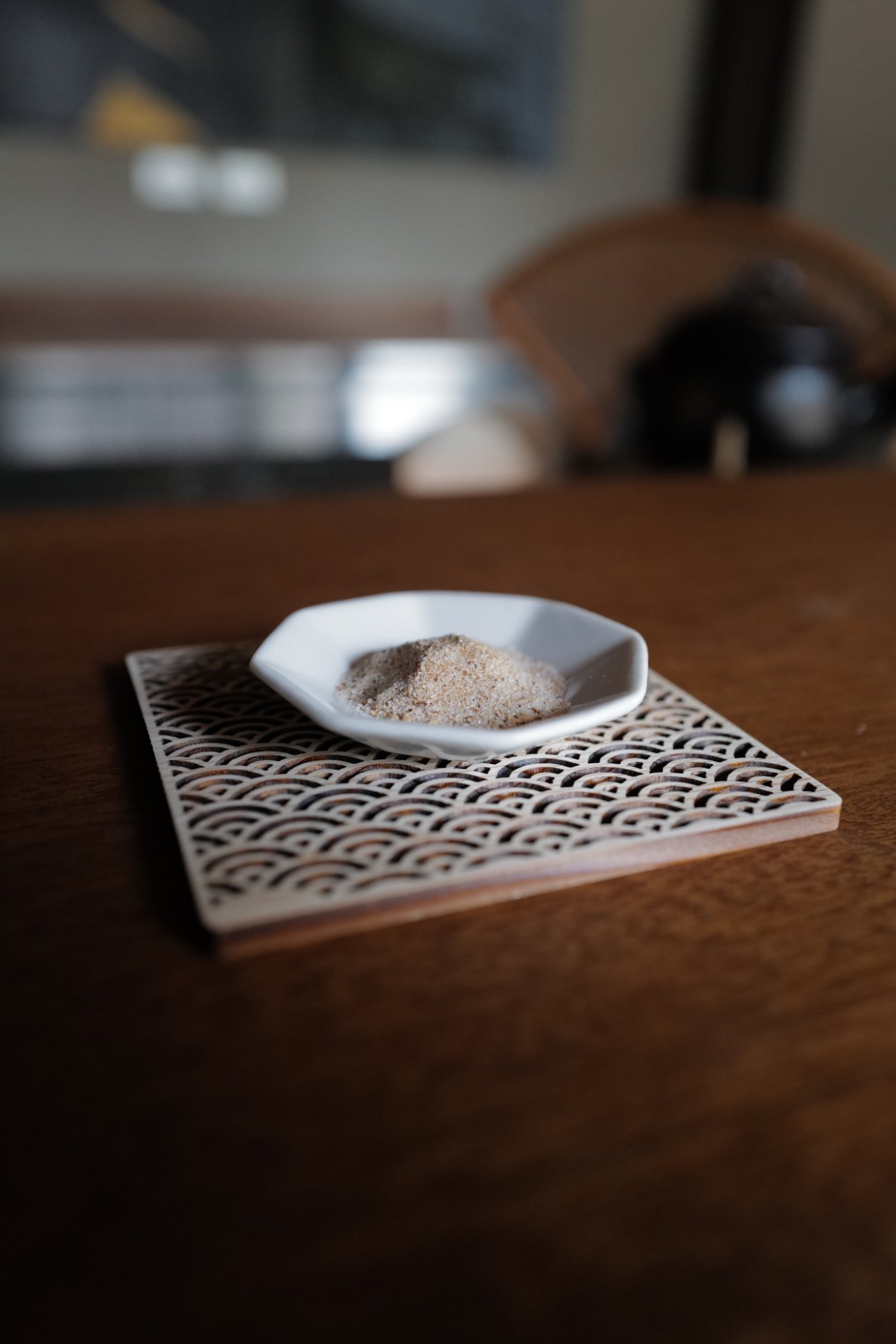 Limited and small batched Dashi from Hiroshima. A small white dish with Japanese Dashi placed on a decorative square mat on a wooden table.