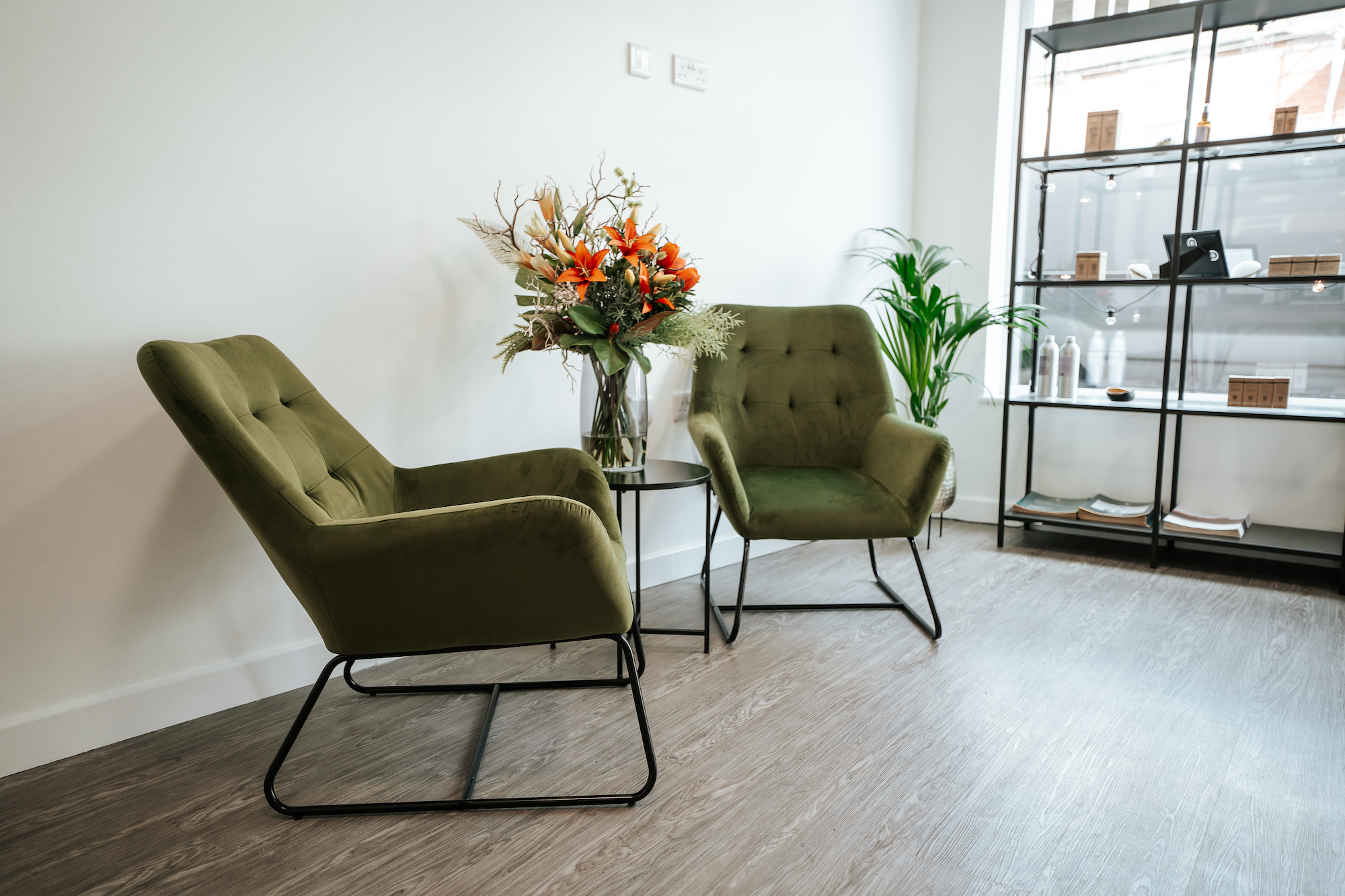 Two velvet green chairs and a table with flowers in a clinic reception area