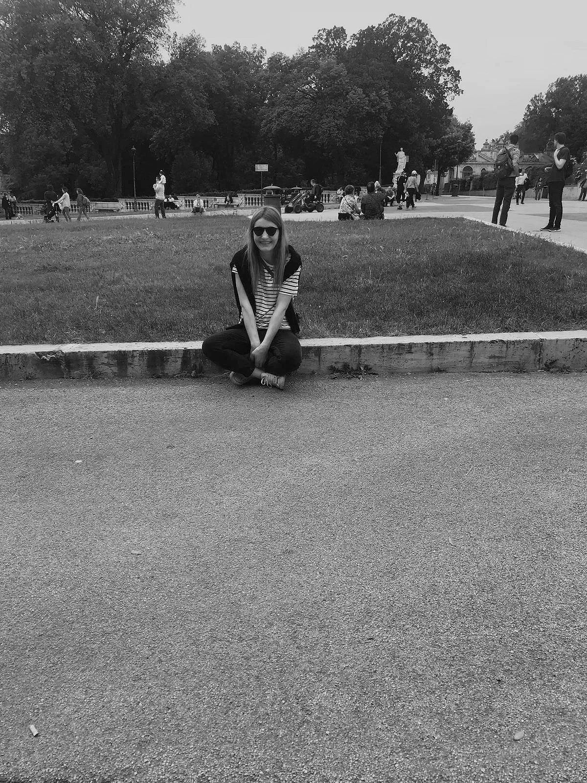 Eva sits on the border of a patch of grass, smiling at the camera