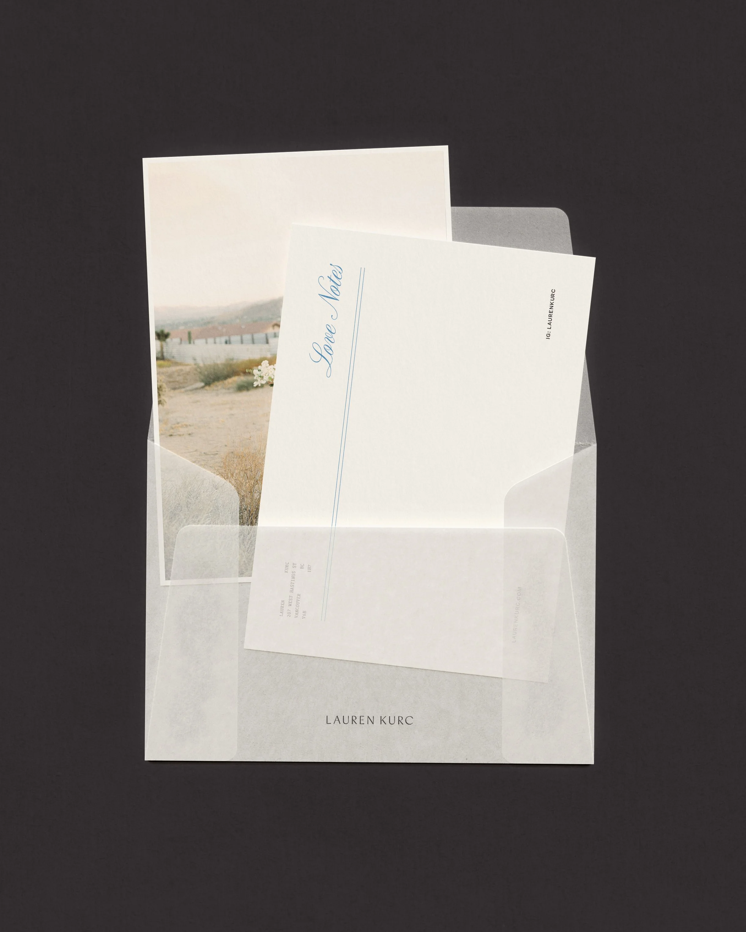 A clear envelope containing a letter with 'Love Note' written on it in blue, a photo of a desert landscape with a fence and mountains in the background. The letter is from Lauren Kurc.