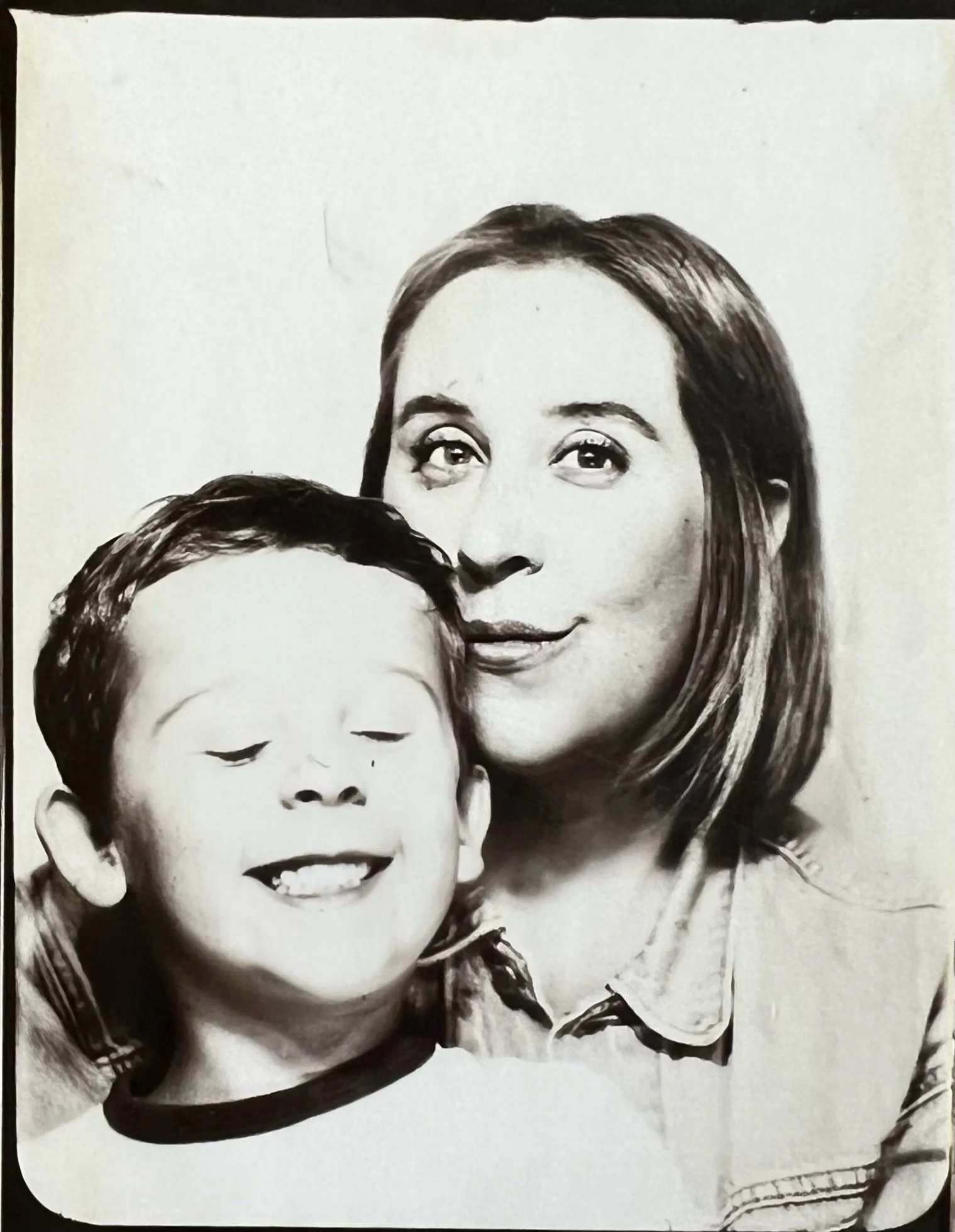 Black and white photograph of a woman with shoulder-length hair and a young boy with short hair, both smiling. The woman has a gentle smile with lips closed, and the boy has a broad smile with eyes closed.
