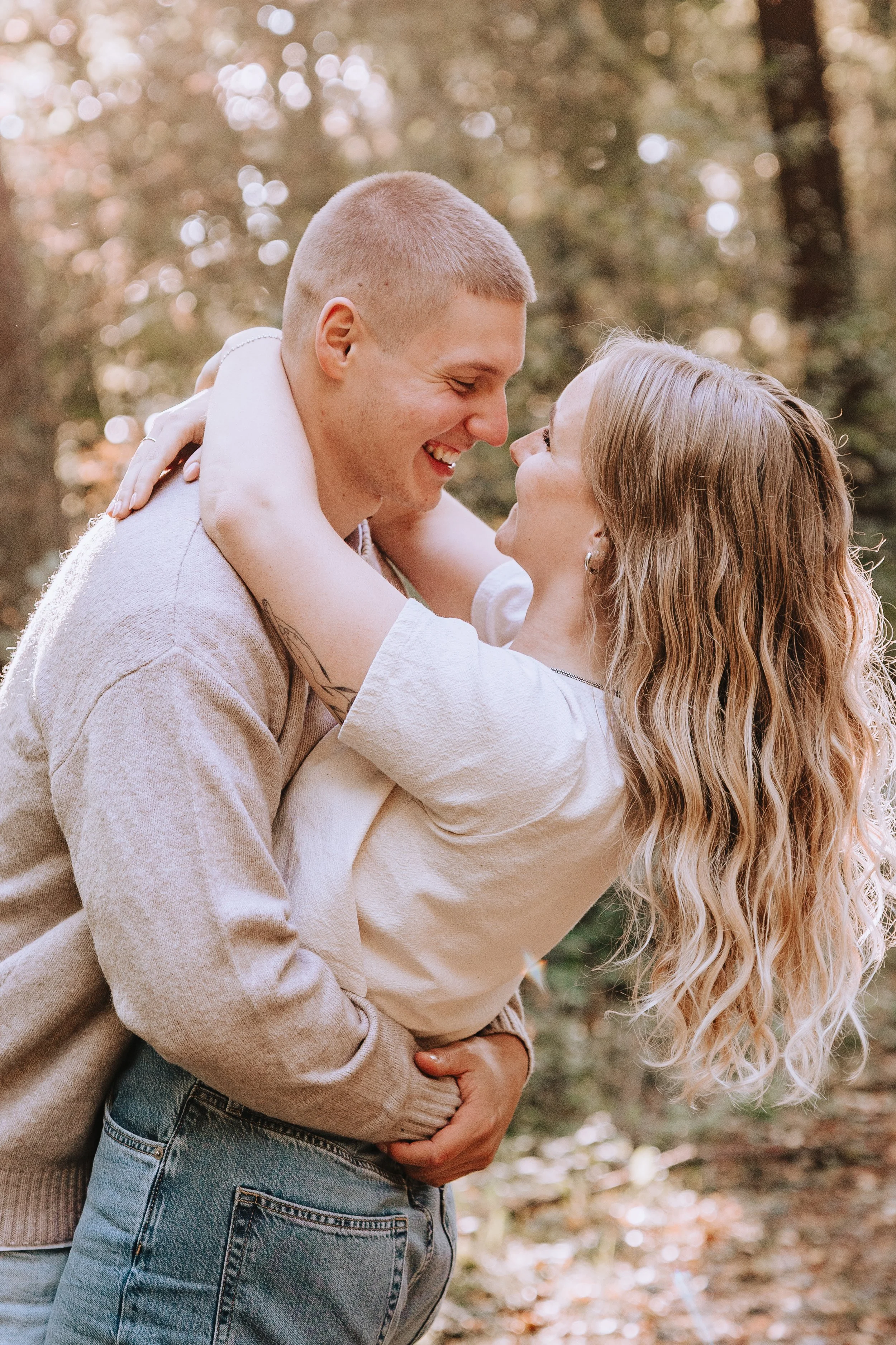 Ein Paar umarmt sich liebevoll im Wald und lächelt sich an.