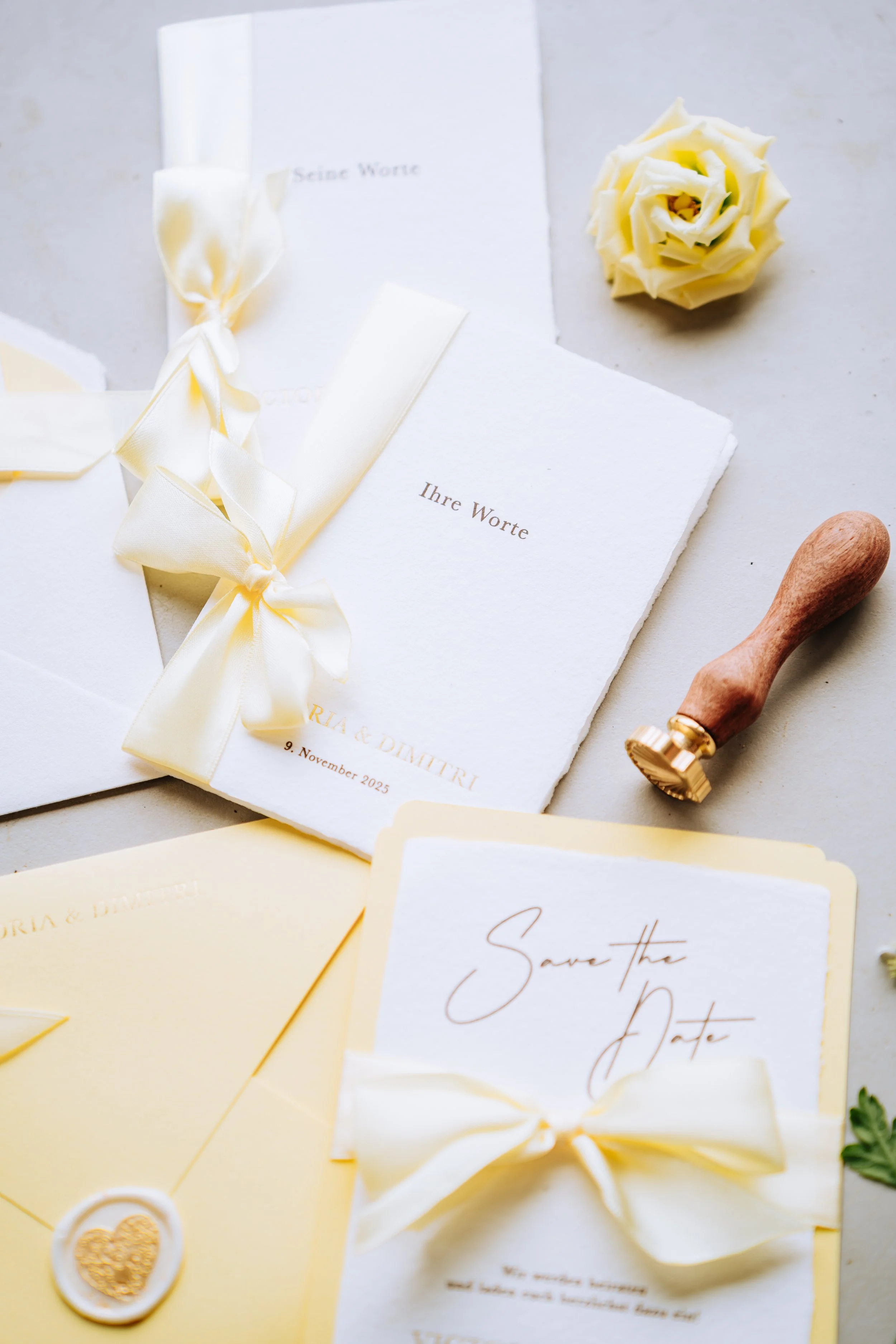 Hochzeitsvorbereitungen mit Einladungskarten, Save-the-Date-Karten, Briefumschlägen, einer weißen Rose, einem Holzstempel und einem Siegel.