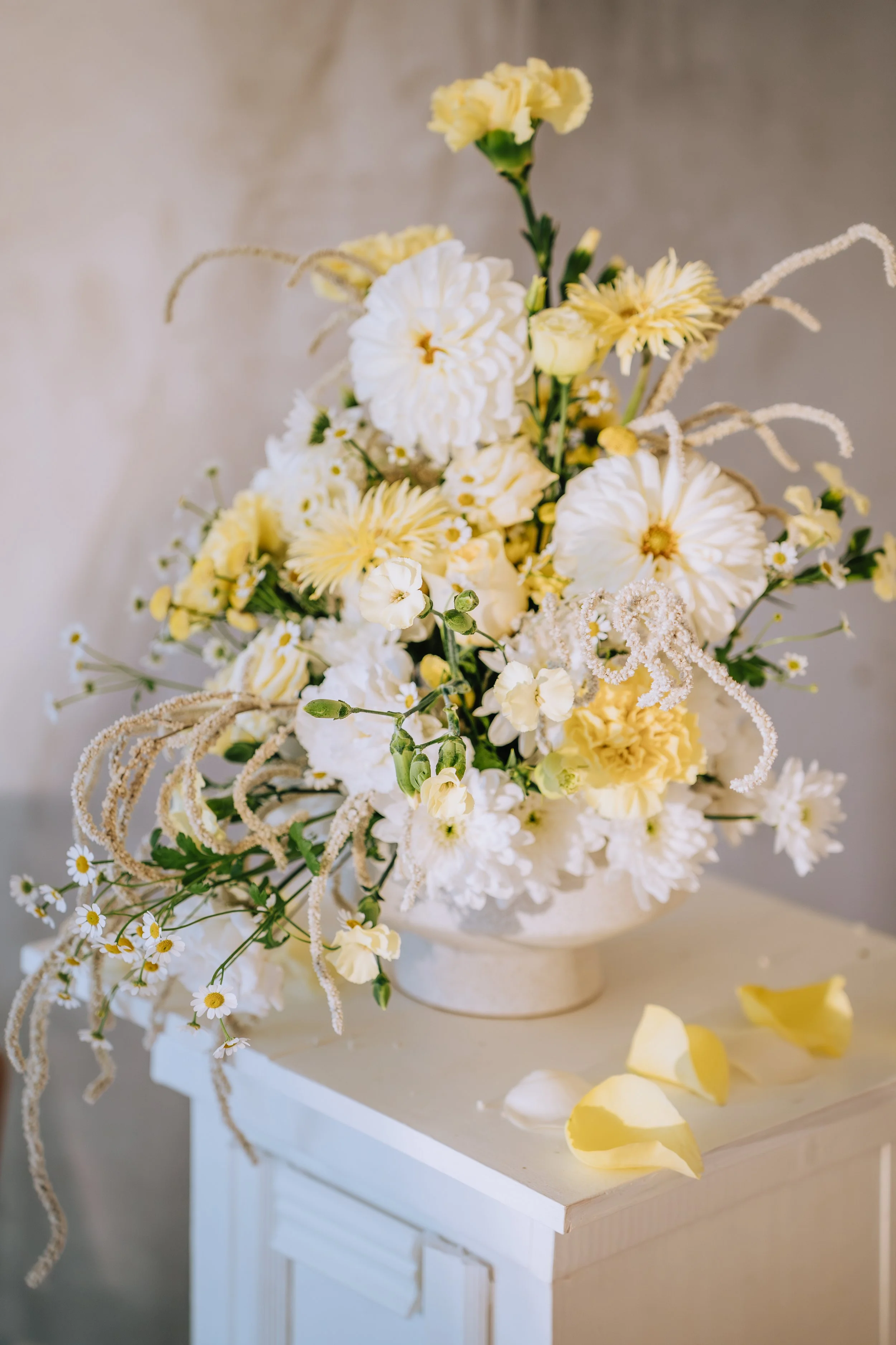 Blumenstrauß mit weißen und gelben Blumen, unterlegt auf einem weißen Möbelstück, mit einigen gelben und weißen Blütenblättern auf der Oberfläche.