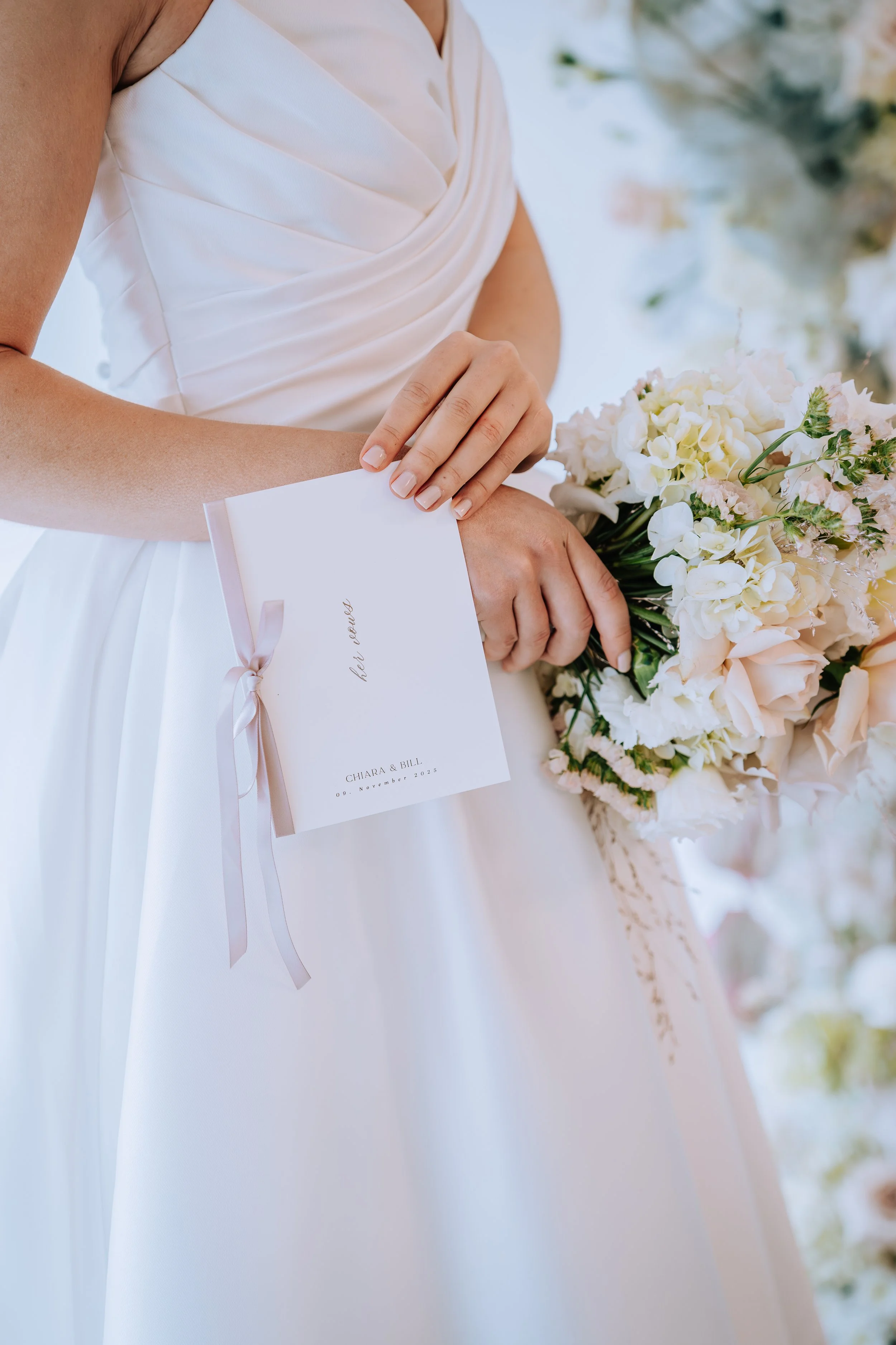 Braut hält einen weißen Hochzeitsstrauß und eine Einladungskarte bei einer Hochzeit.