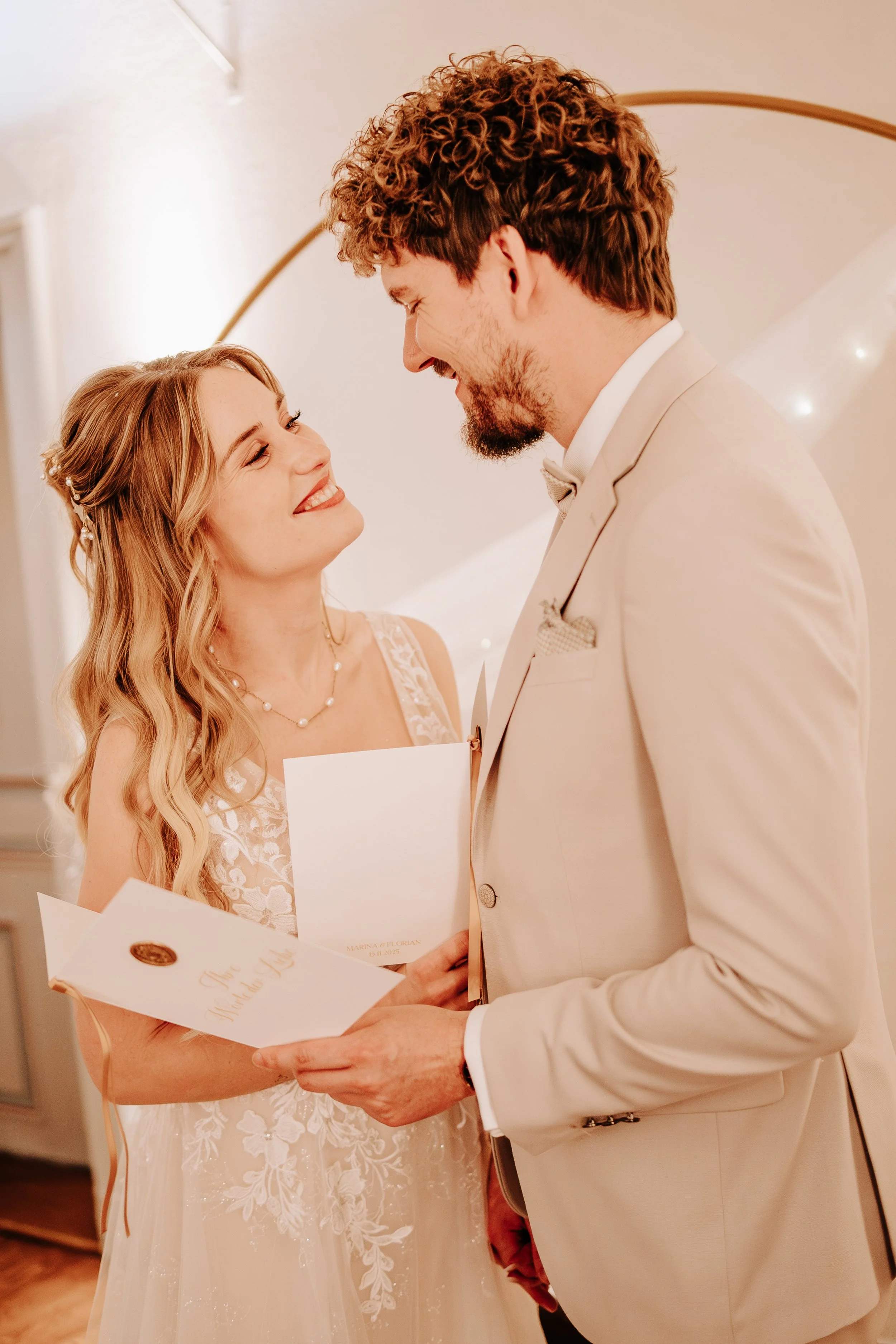 Hochzeitszeremonie mit Braut und Bräutigam, die sich gegenseitig liebevoll ansehen, während sie Gelübde austauschen in einem eleganten, hellen Raum.