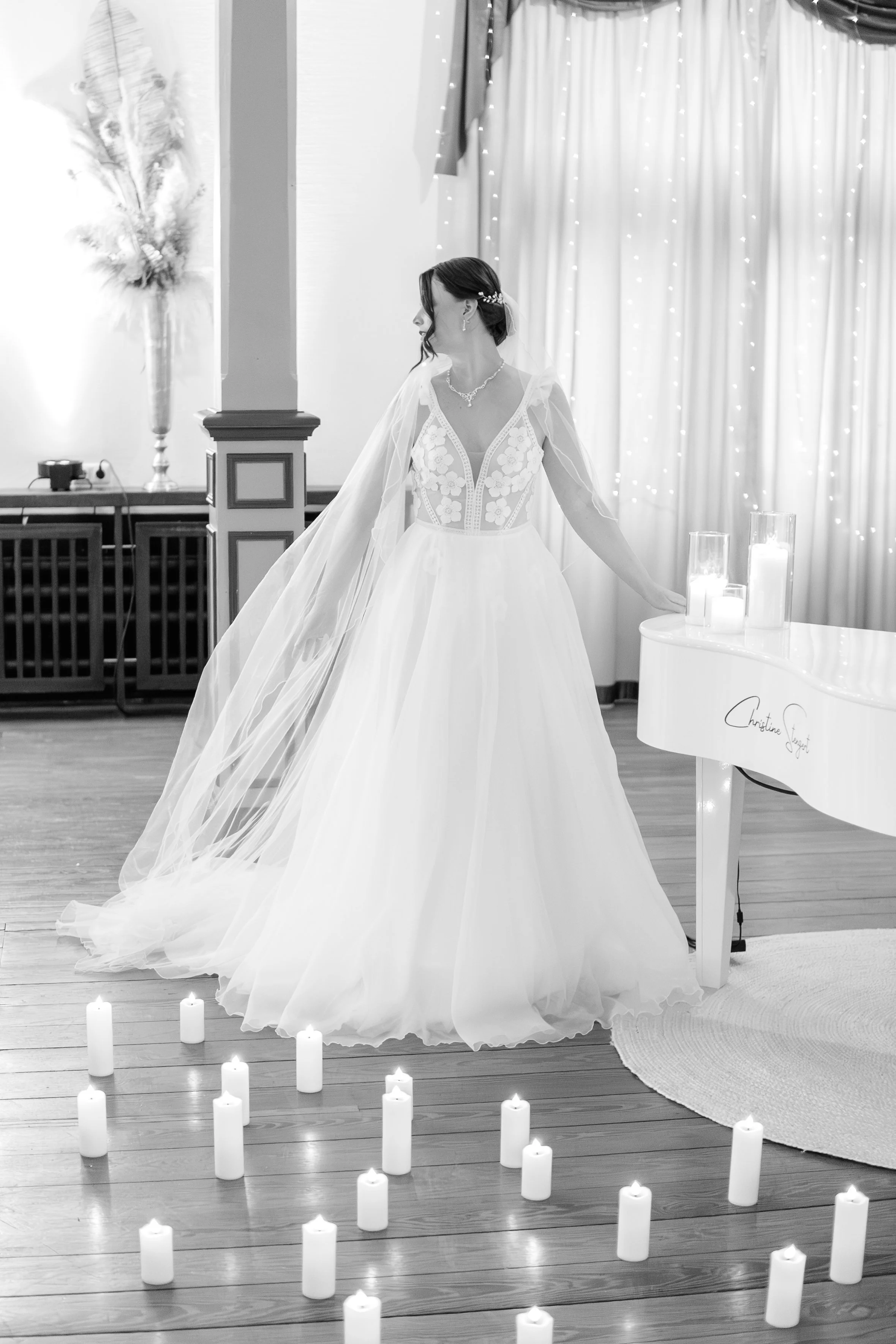 Braut in Hochzeitskleid und Schleier steht in einem festlich dekorierten Raum, umgeben von Kerzen.