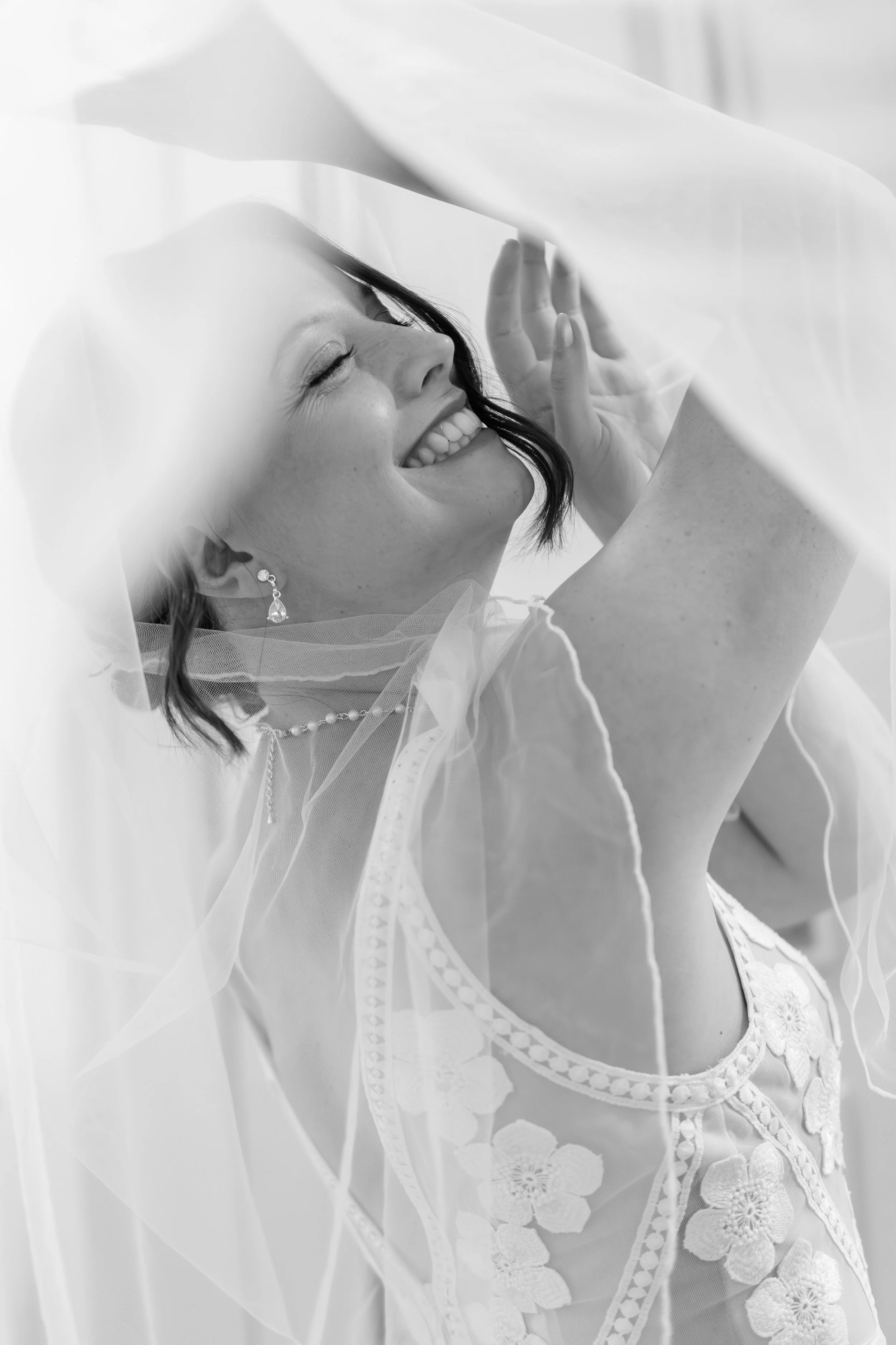 Junge Frau in Brautkleid, lachend, Gesicht zur Seite, hinter einem durchsichtigen Schleier.