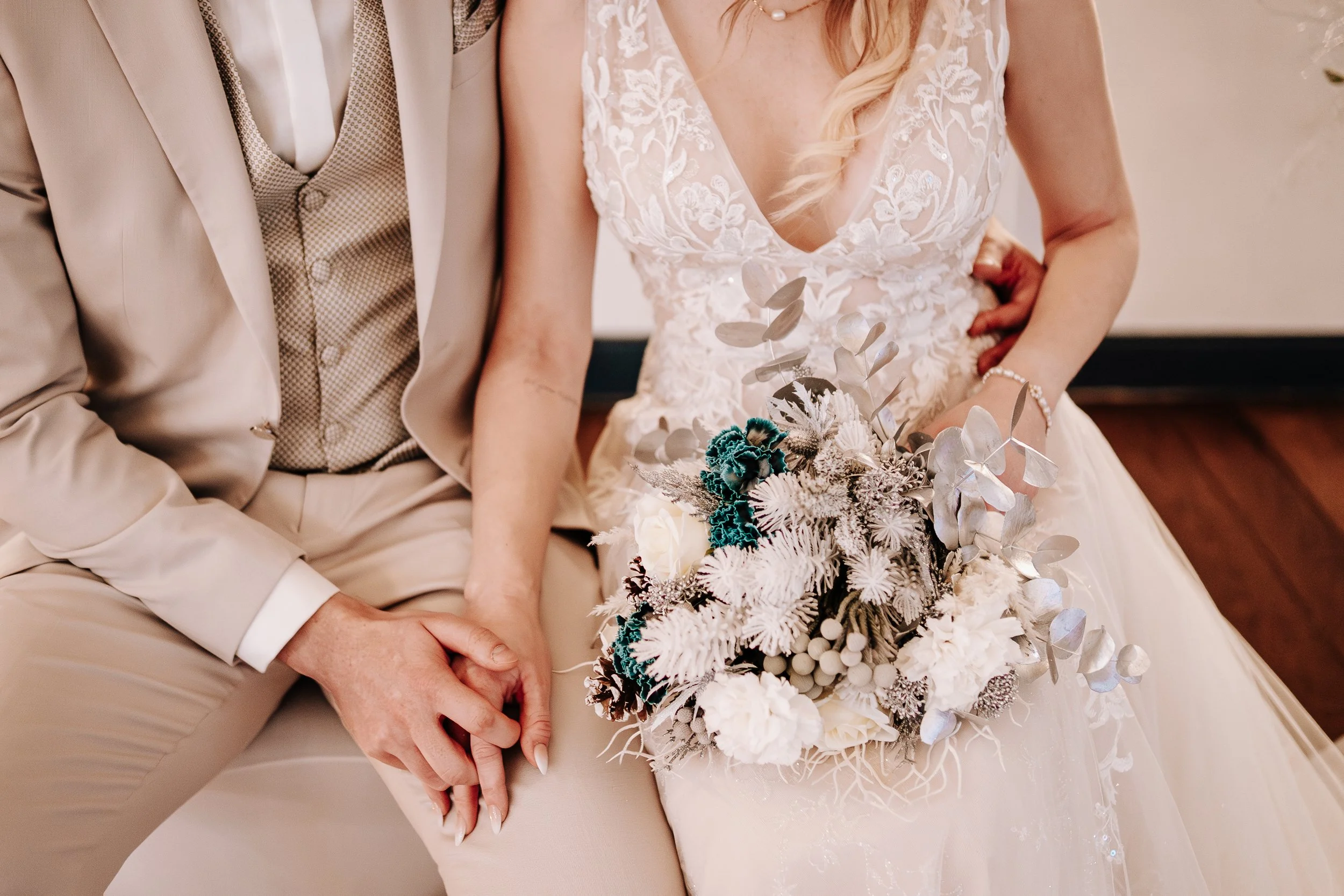 Hochzeitspaar sitzt zusammen, die Braut hält einen Blumenstrauß, beide ausschließlich von der Taille aufwärts sichtbar.