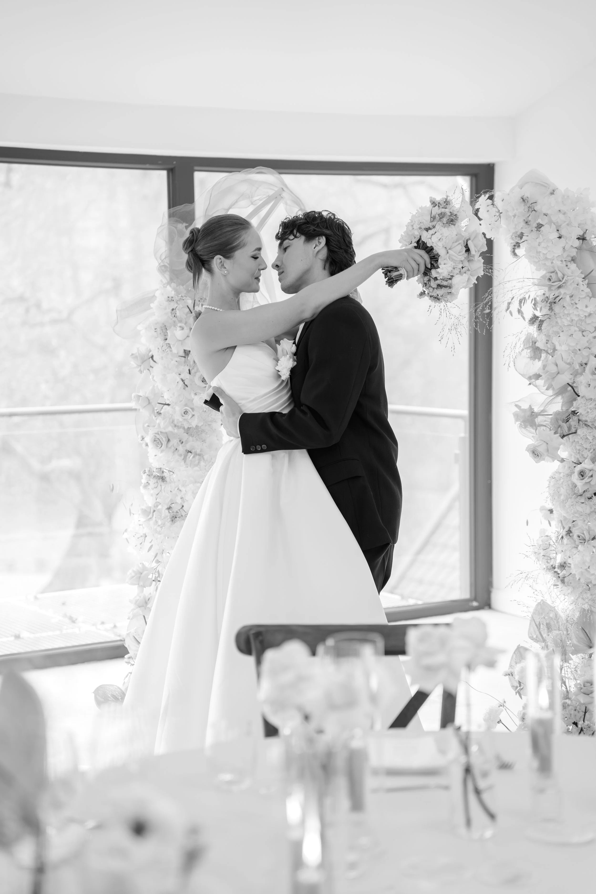 Braut und Bräutigam während der Hochzeit, die sich in die Augen schauen, mit Blumenhochzeit im Hintergrund, schwarz-weiß Foto.
